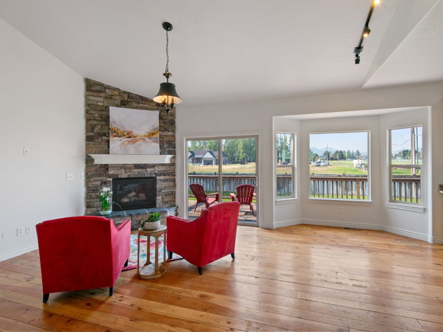 Living space featuring a stone fireplace with a mantel, wood-finish flooring, and a bay window