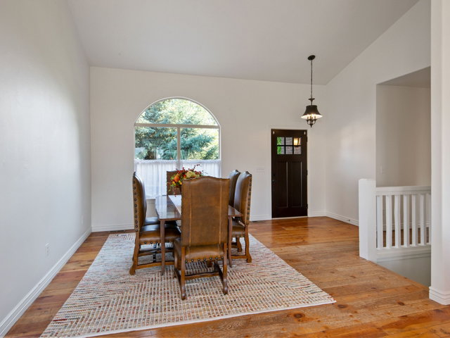 Vaulted ceiling dining area featuring wood-finish flooring, an arched window, and a dark wood entry door with glass panels