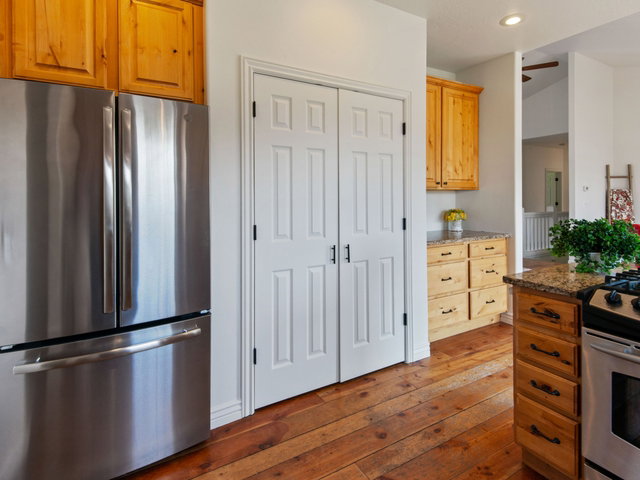 Kitchen featuring stainless steel appliances, natural wood cabinetry, wood-finish flooring, granite countertops, and white paneled pantry doors