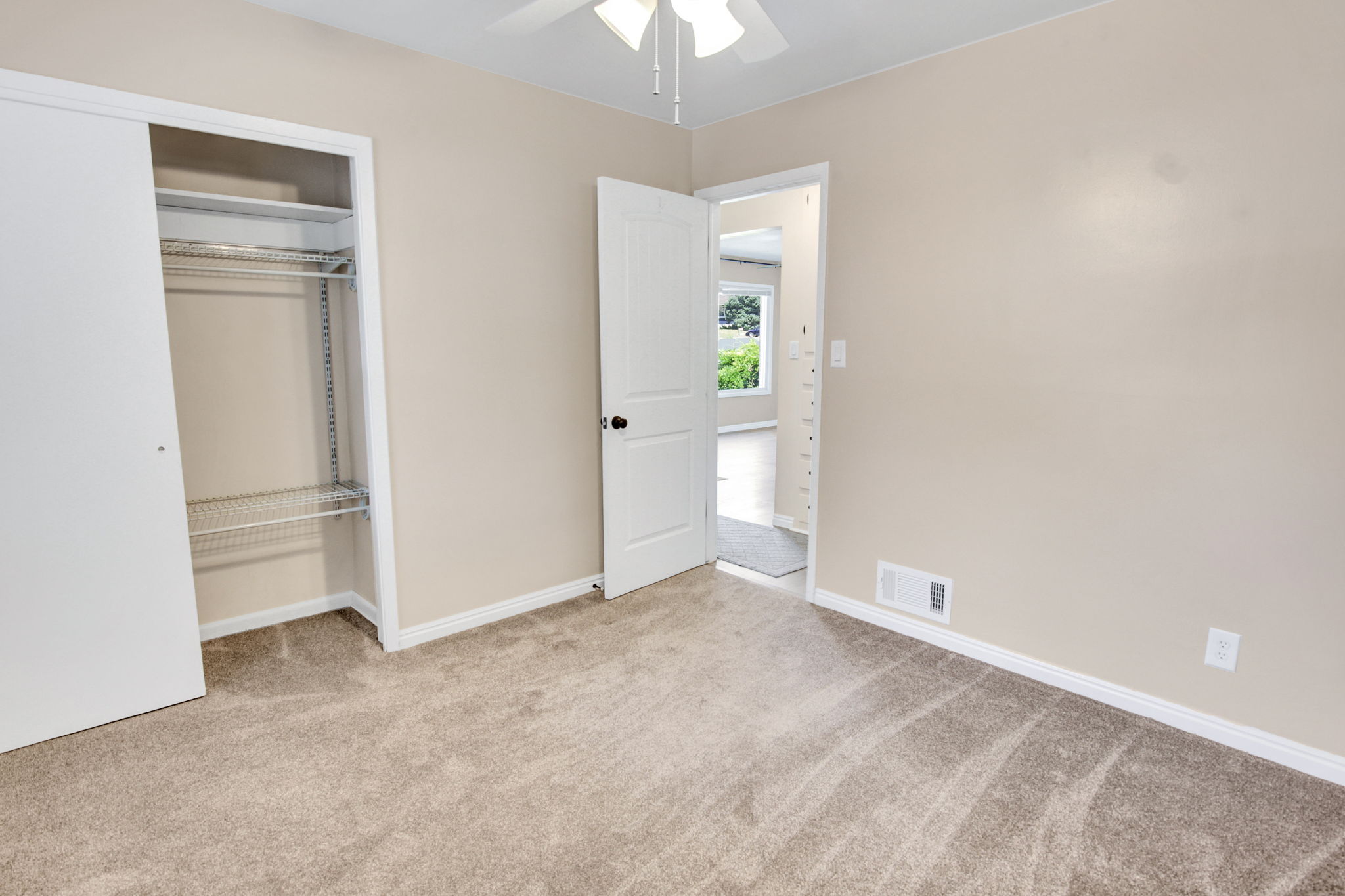 Carpeted interior space featuring a ceiling fan, neutral wall paint, white trim, and a closet with sliding doors and wire shelving