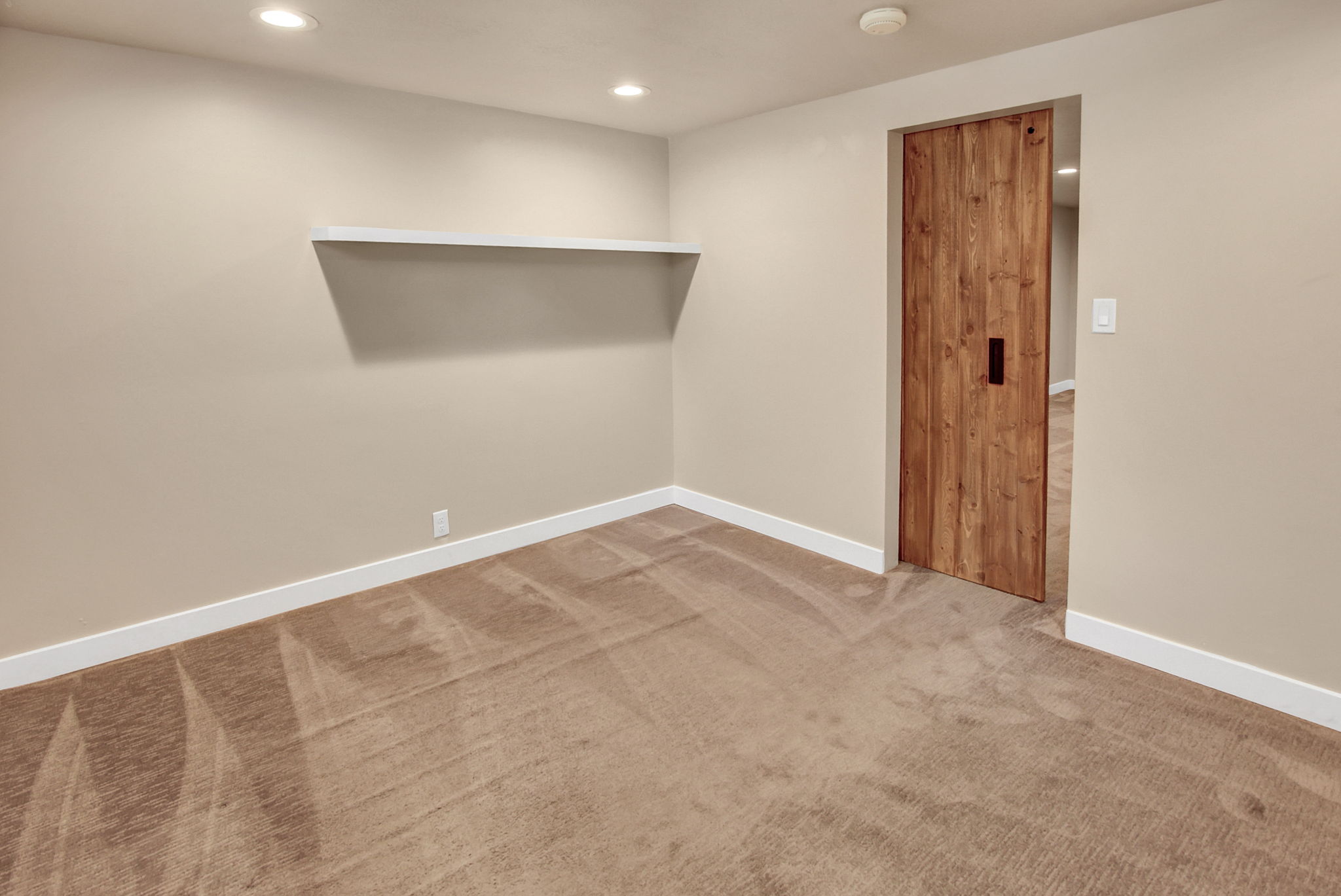 Room featuring neutral wall tones, recessed lighting, a floating wall shelf, and a contemporary wood panel door with a dark pull handle