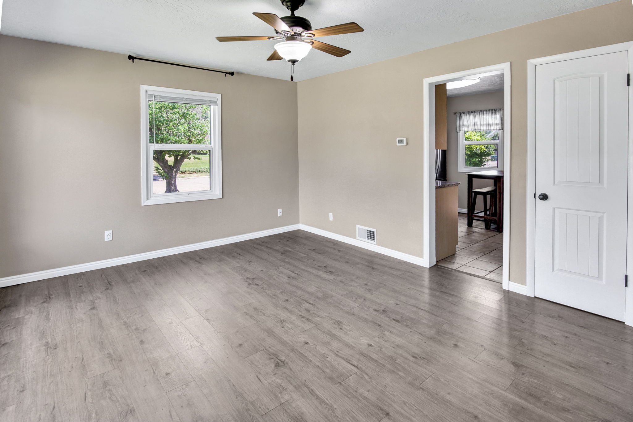 Spacious room featuring wood-finish flooring, a ceiling fan with integrated lighting, and a white window frame