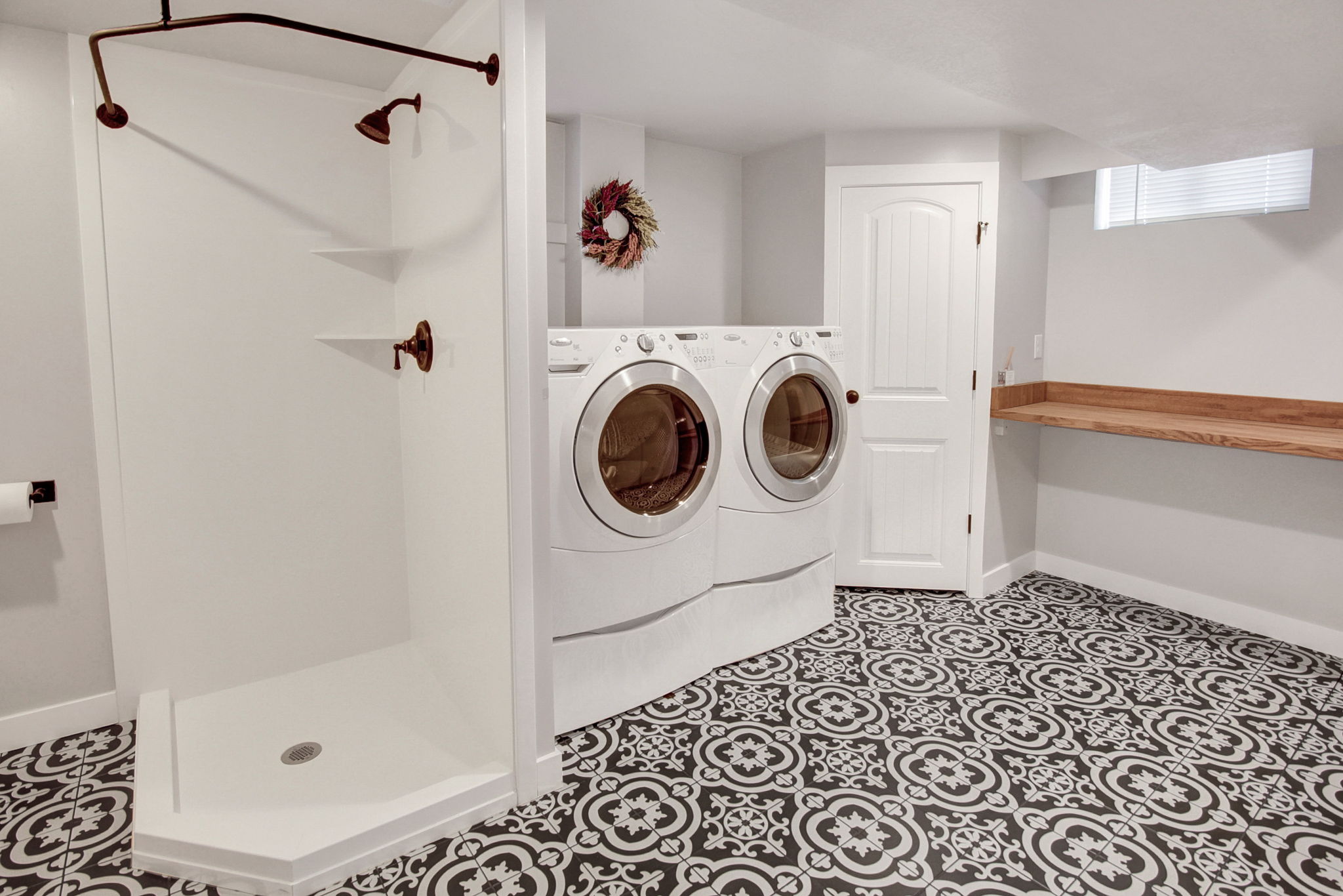 Utility area with patterned floor tiles, a corner shower, and a built-in wood-finish countertop