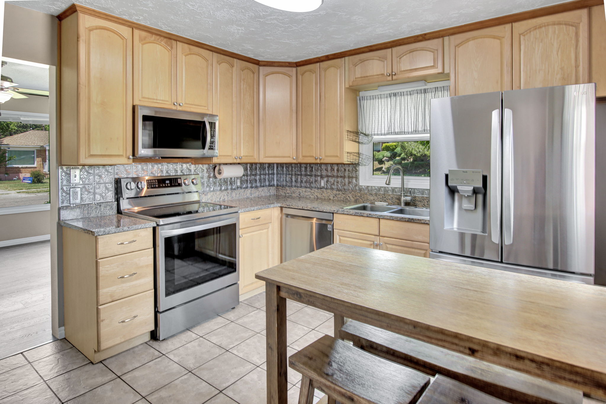 Kitchen featuring light wood cabinetry, stainless steel appliances, granite countertops, a tiled backsplash, and ceramic tile flooring