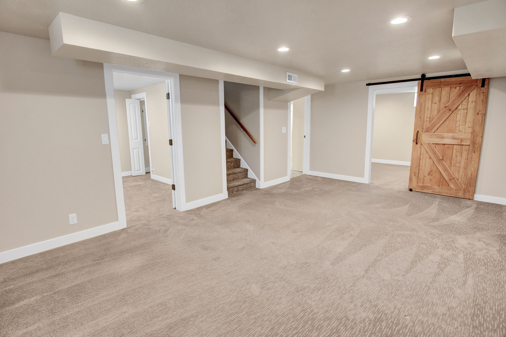 Spacious room with neutral-toned carpeting, recessed lighting, a built-in staircase, and a rustic wood-finish barn door