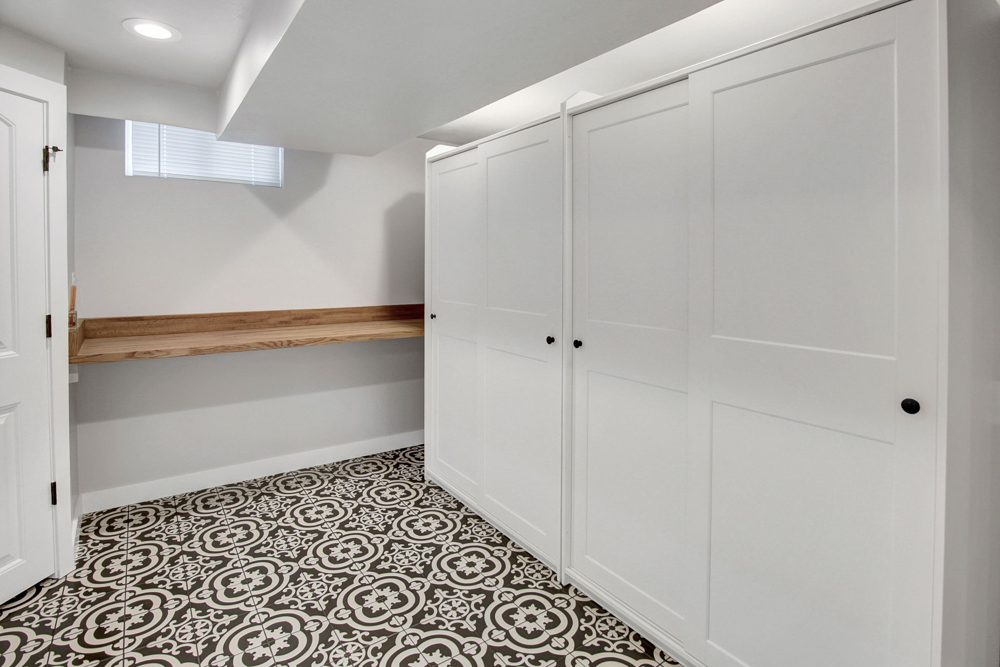 Patterned tile flooring, built-in white cabinetry with matte black hardware, and a wood-finish floating shelf