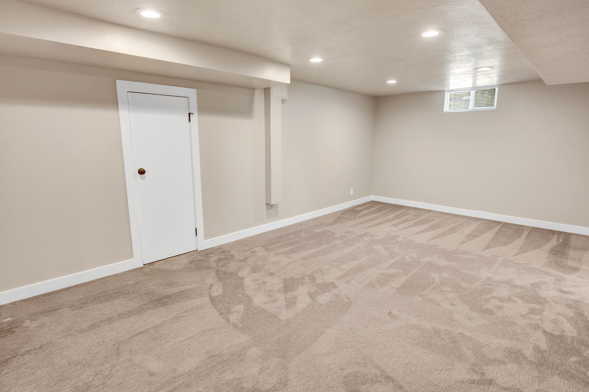 Spacious room featuring neutral carpeting, recessed ceiling lighting, a white door with a round knob, and a high-set window