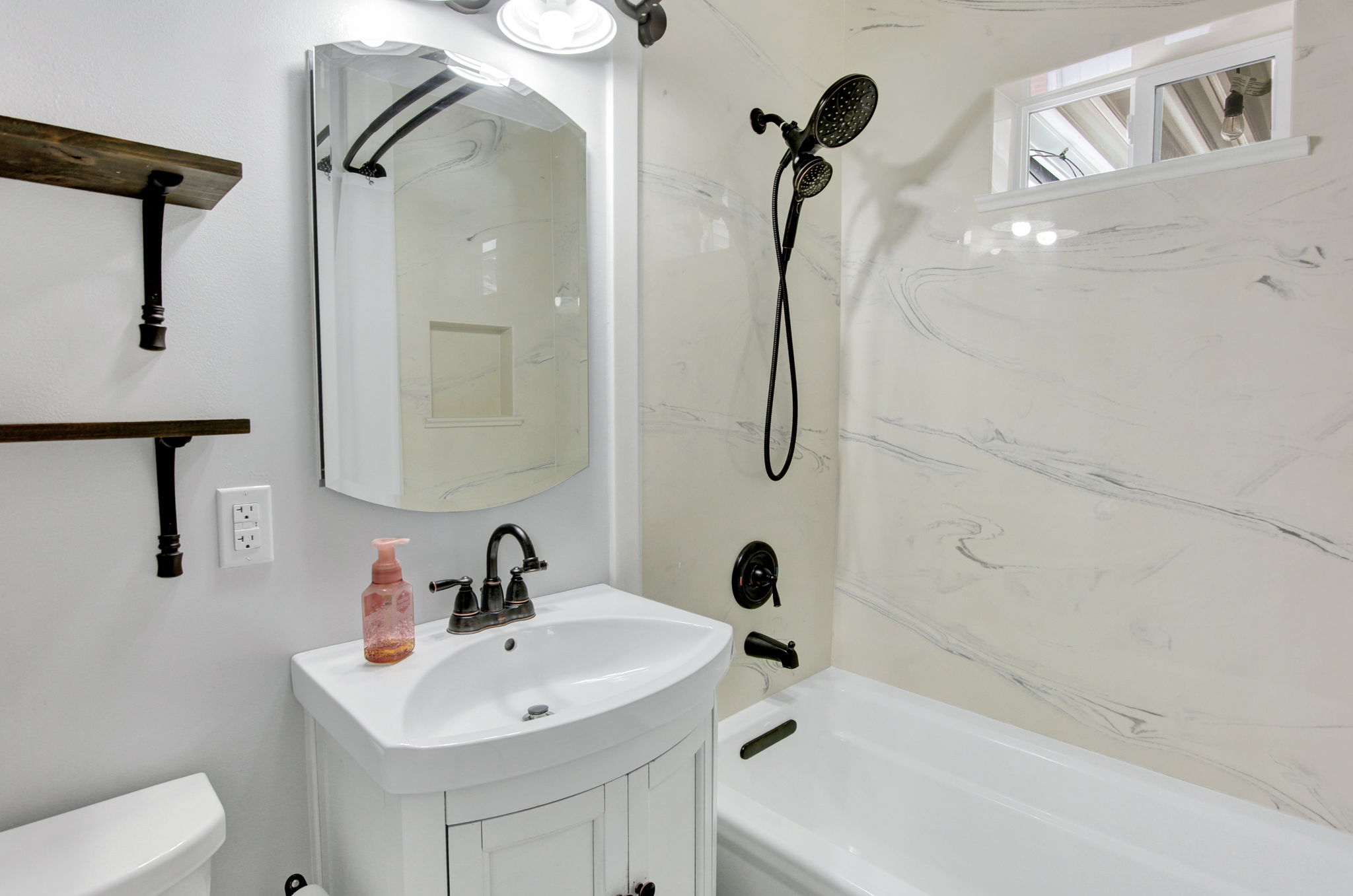 Contemporary bathroom featuring a white vanity with integrated sink, black-finish plumbing fixtures, and two rustic wood-finish floating shelves