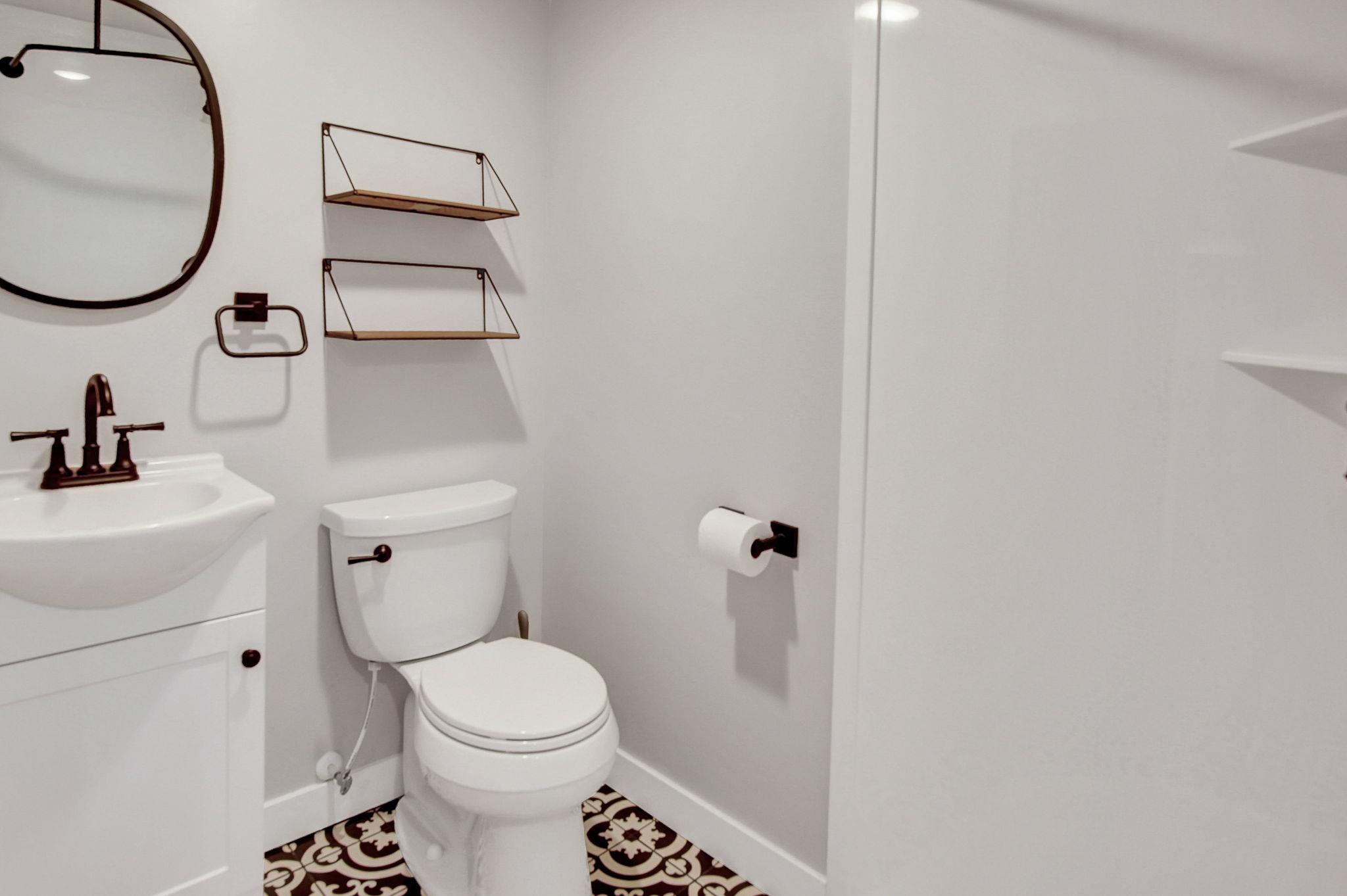 Bathroom featuring decorative floor tiling, a white vanity with an integrated sink, dark bronze fixtures, and two wall-mounted shelving units
