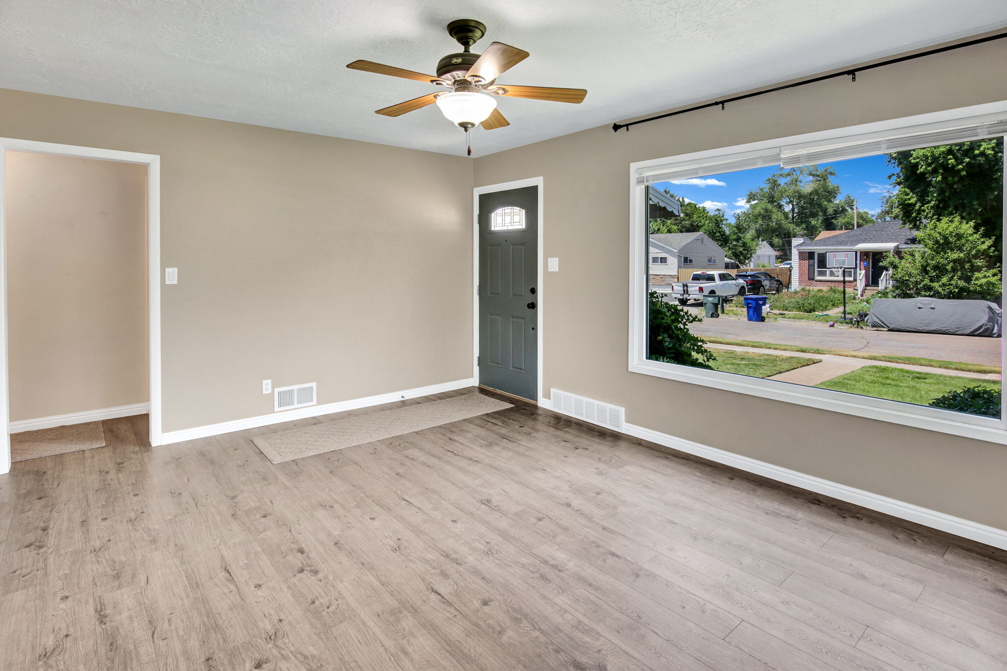 Spacious room featuring wood-finish flooring, a large picture window, neutral wall paint, and a ceiling fan with integrated lighting