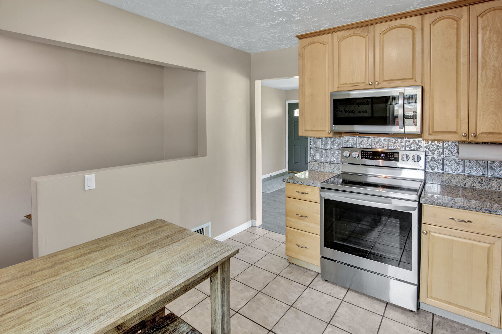 Kitchen featuring light wood cabinetry, granite-finish countertops, stainless steel appliances, and a tiled backsplash
