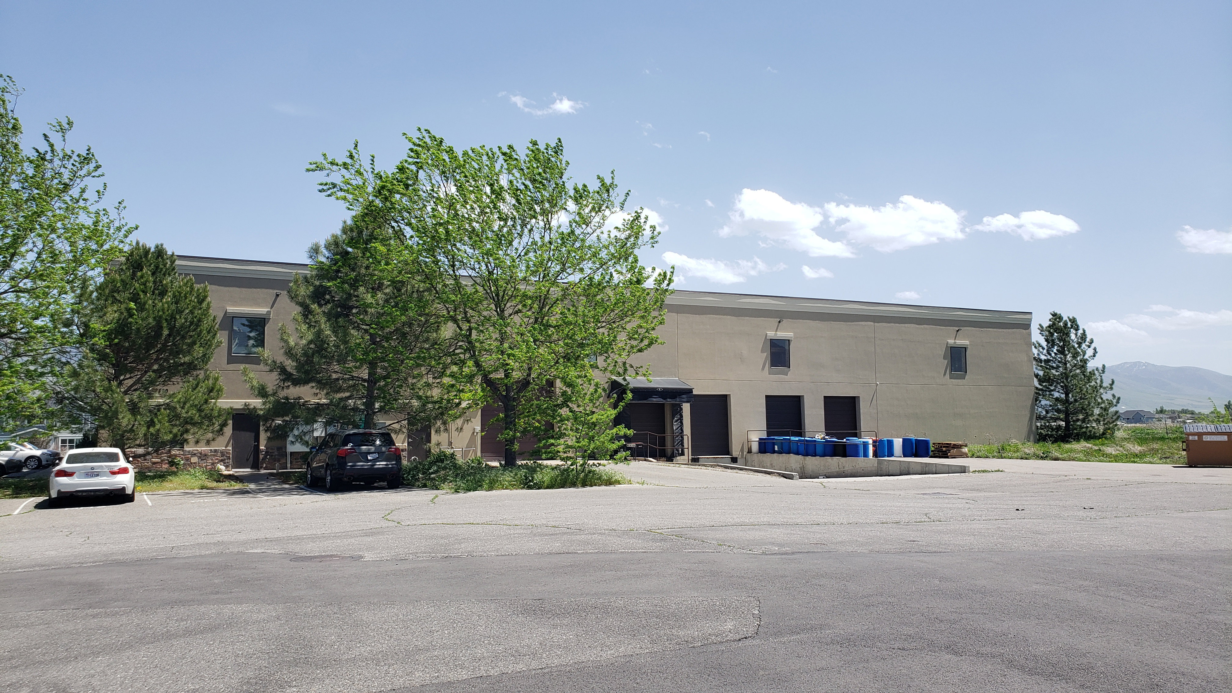 Commercial building featuring a large paved parking area, multiple roll-up doors for access, and a loading dock