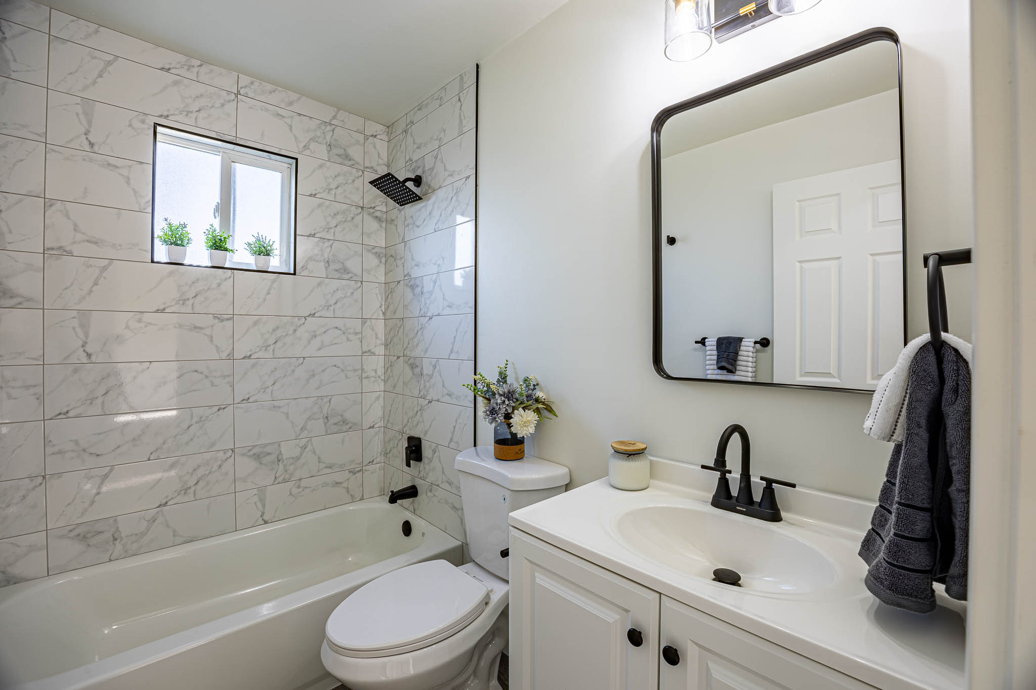 Full bathroom featuring a white vanity with integrated sink, matte black fixtures, a rectangular framed mirror, and a tiled shower-tub combination with a rain showerhead