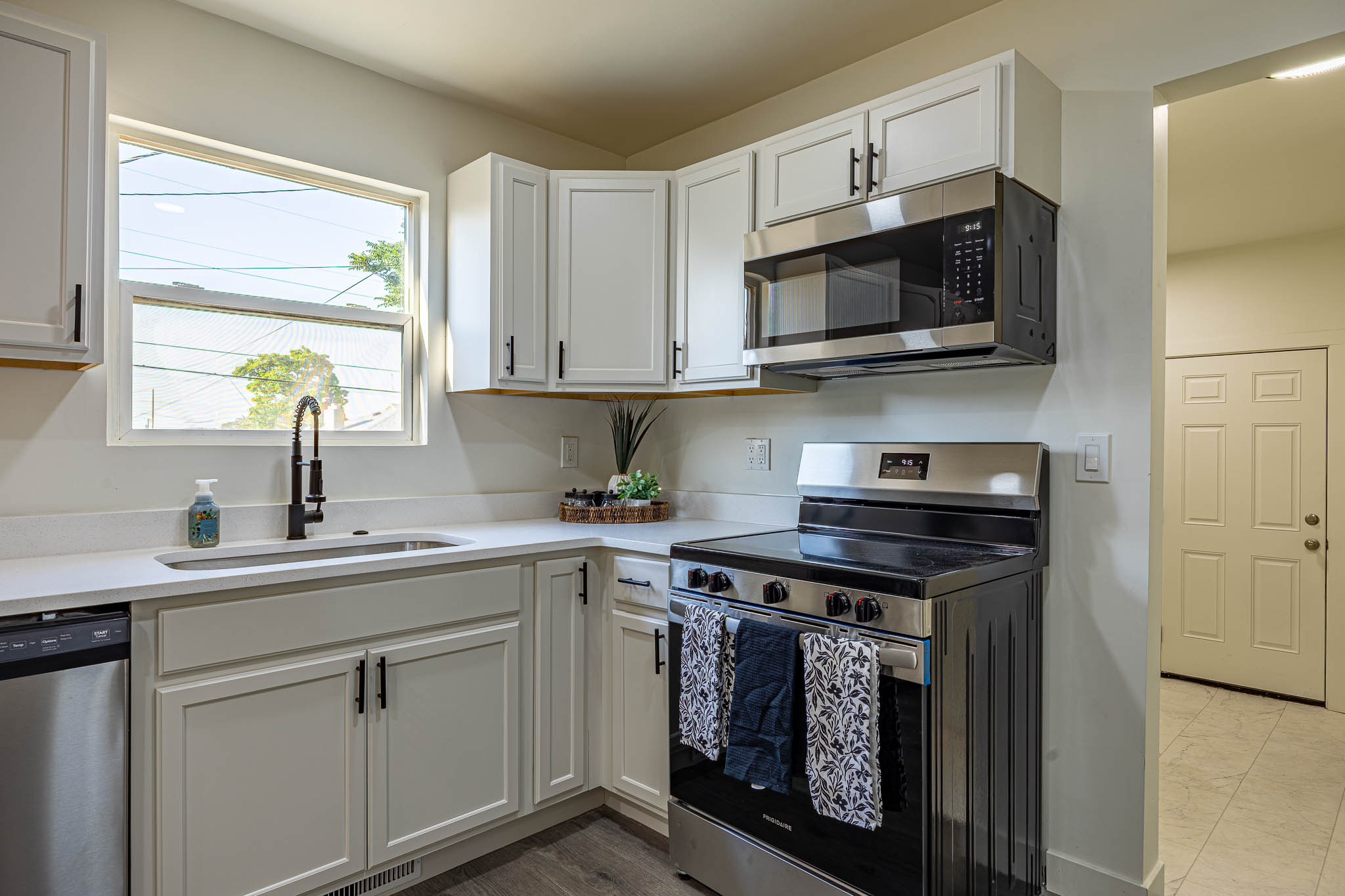 Contemporary kitchen featuring white cabinetry with black hardware, stainless steel appliances, a window above the sink, and light-toned countertops