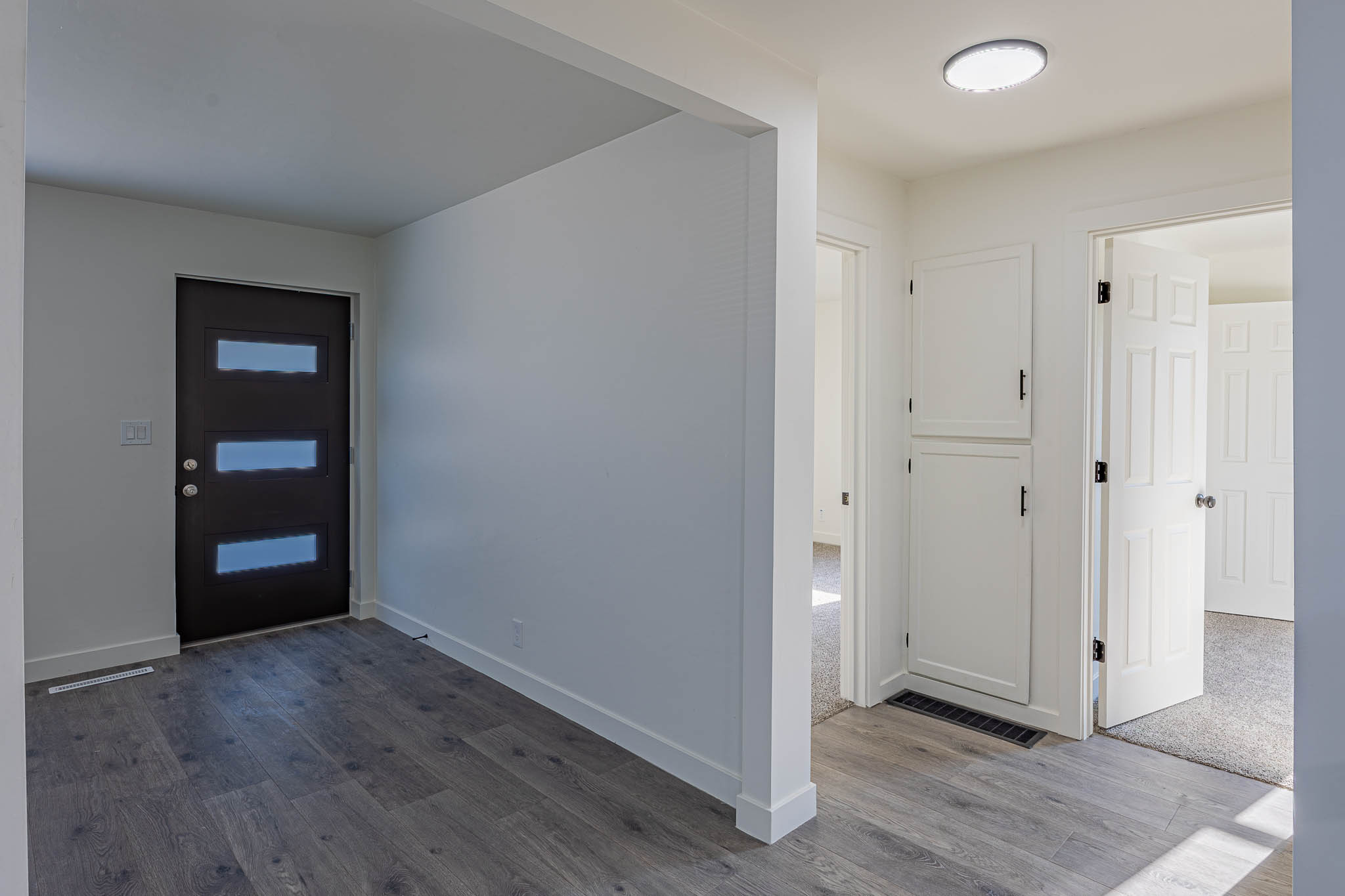 Entryway featuring wood-finish flooring, a contemporary front door with horizontal glass inserts, white baseboards, and a built-in white cabinet with black hardware