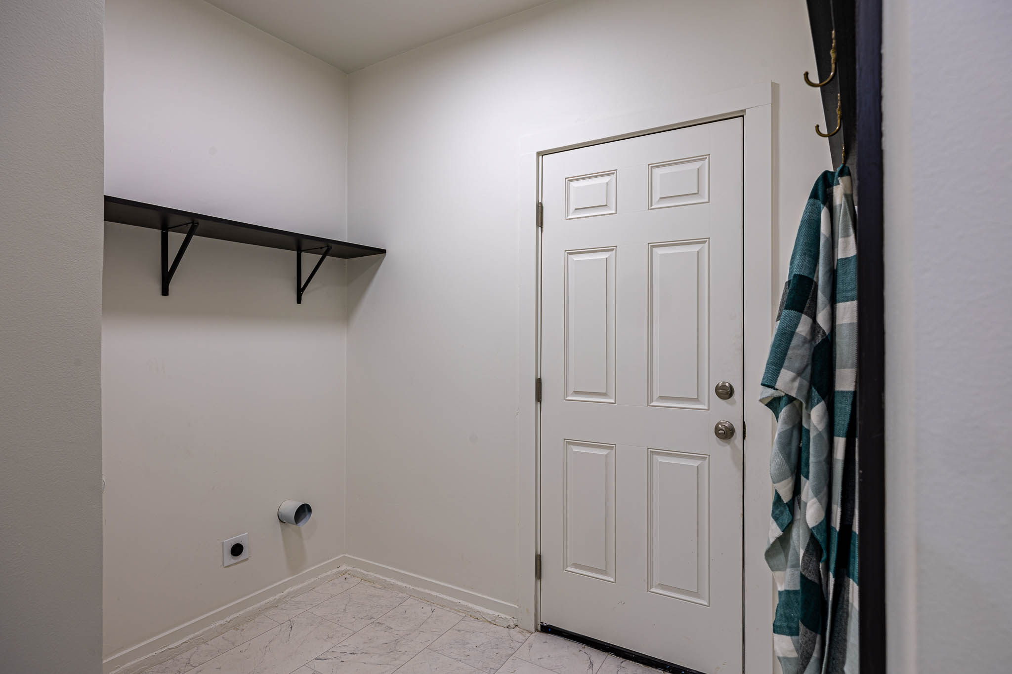 Dedicated utility space featuring a five-panel entry door with brushed nickel hardware, light-toned tile flooring, and a built-in wall shelf with black metal brackets