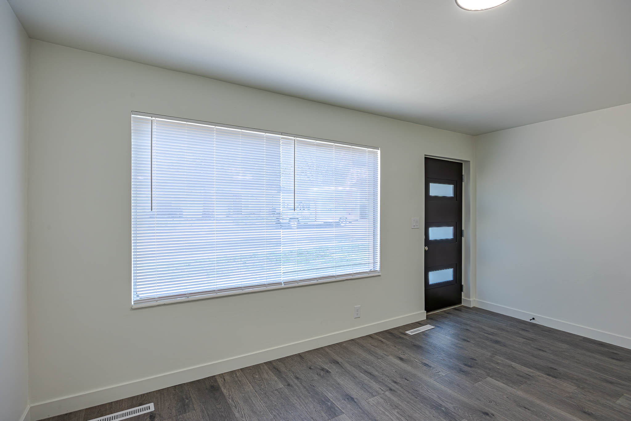 Spacious room featuring wood-finish flooring, white baseboards, and a modern entry door with frosted glass panels