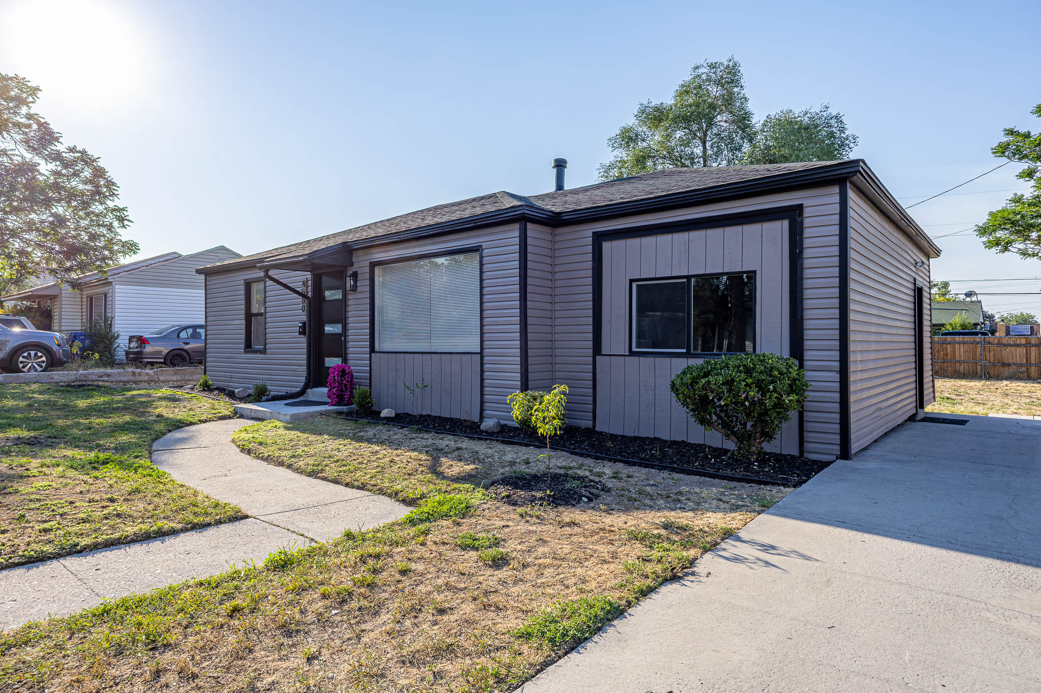 Single-story residence featuring light gray siding with dark trim, a covered front entry, a concrete walkway, and a concrete driveway