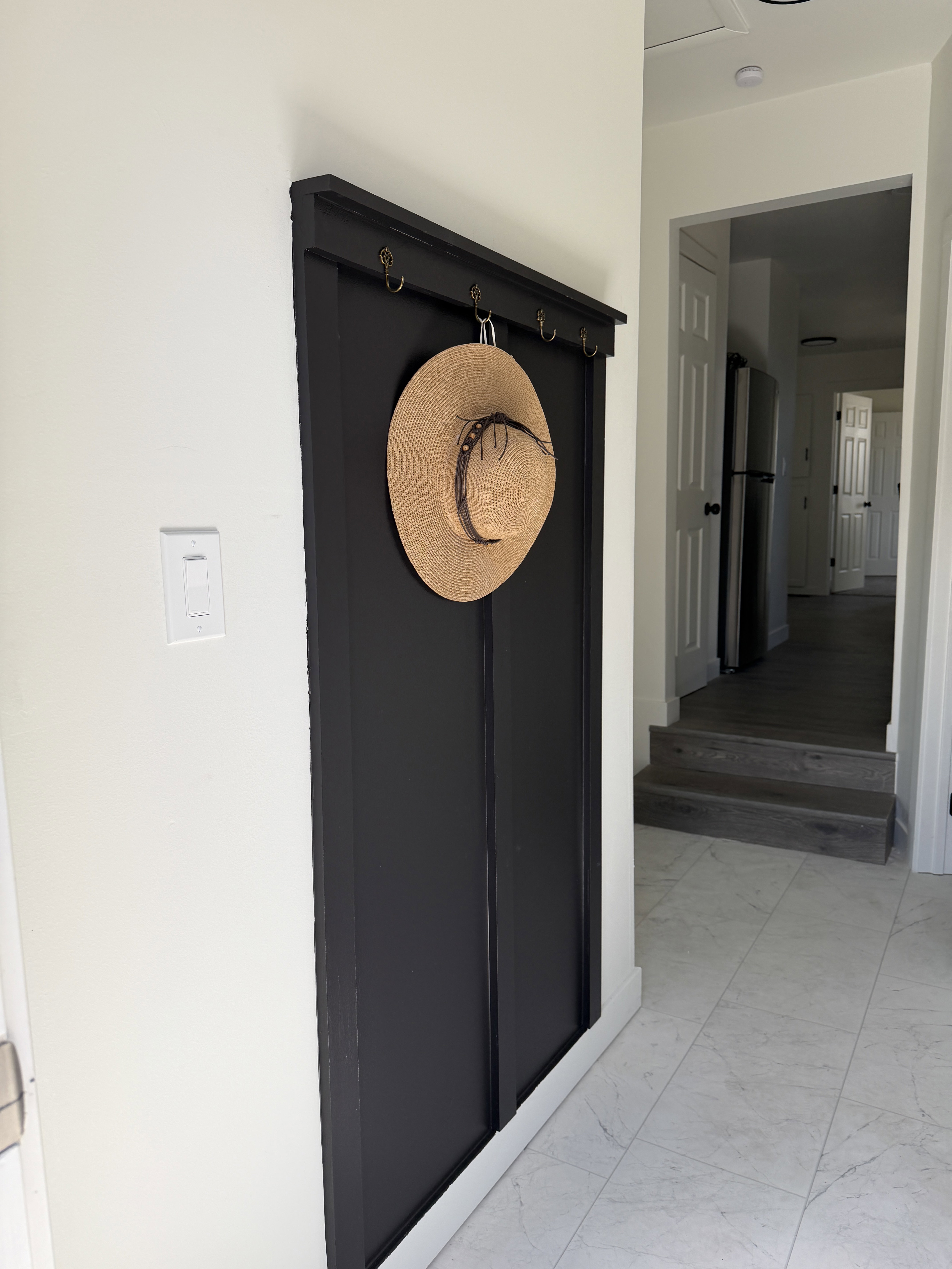 Entryway featuring light-toned tile flooring and a built-in black coat rack with brass-toned hooks