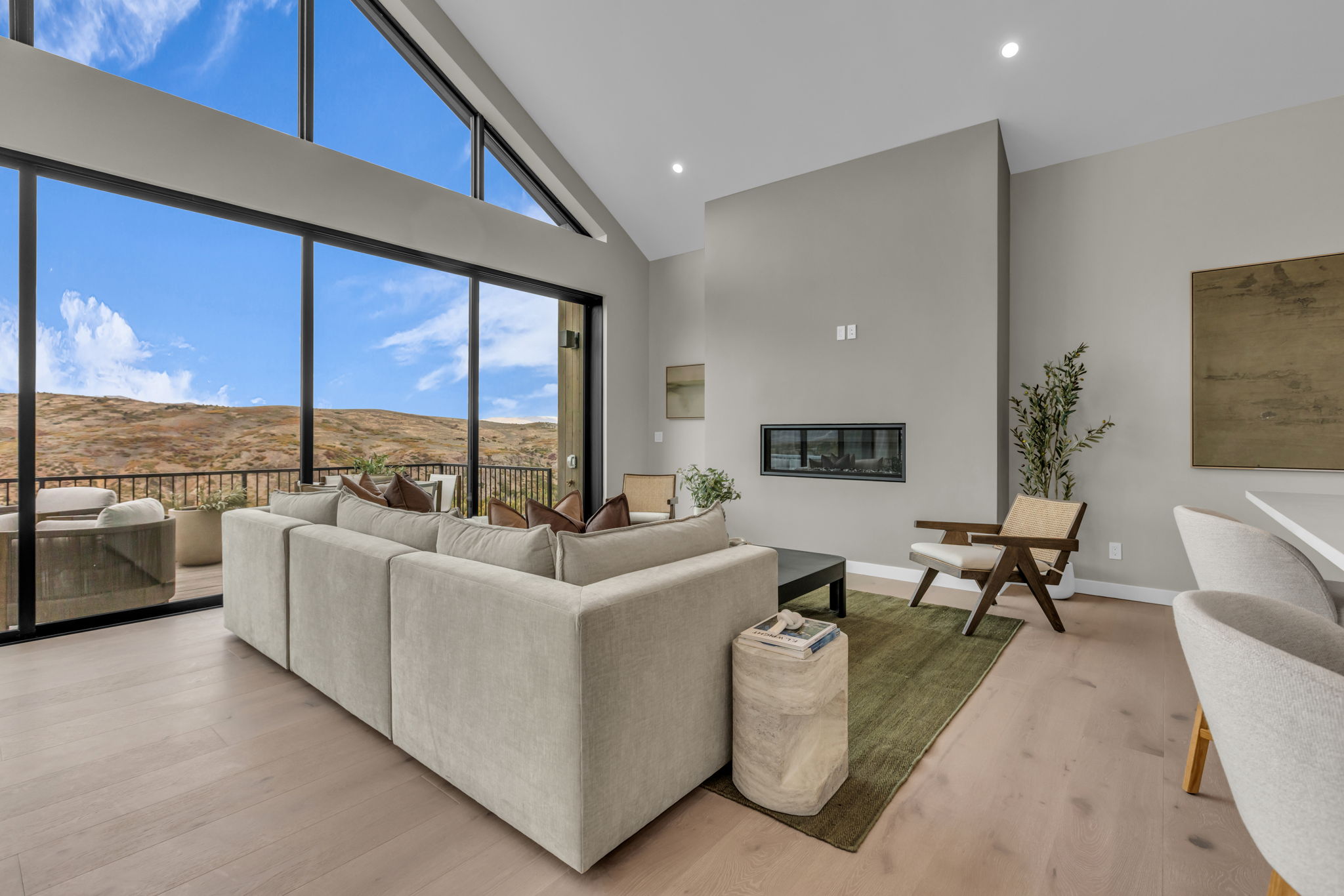 Spacious living area featuring expansive floor-to-ceiling windows, vaulted ceilings, a modern linear fireplace, recessed lighting, and light wood-finish flooring