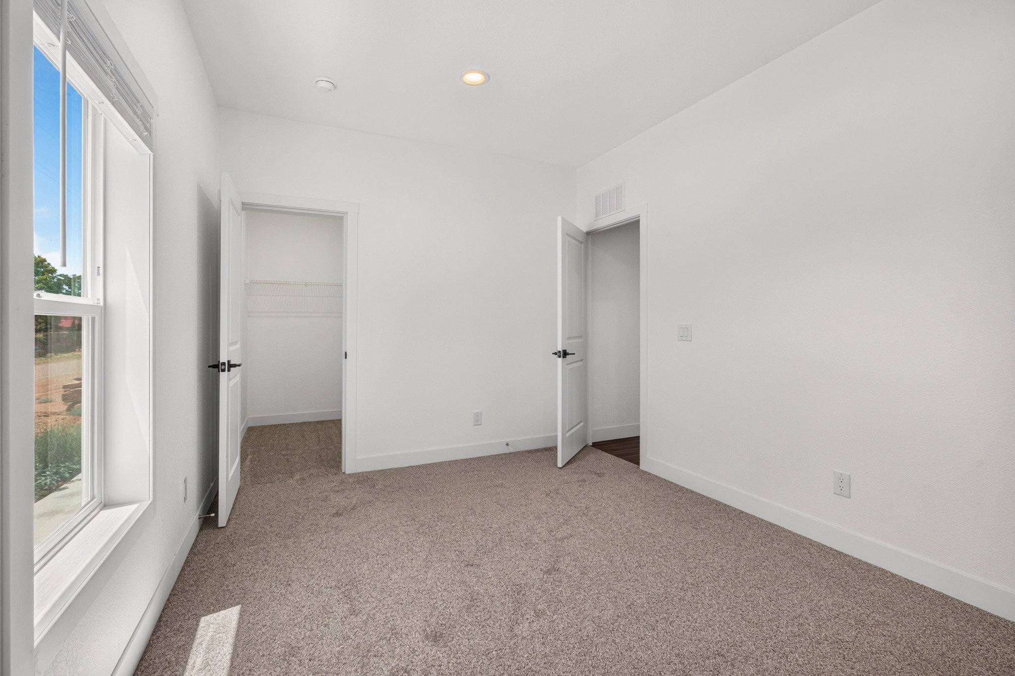 Carpeted room with white walls, a large window, recessed lighting, and two interior doors