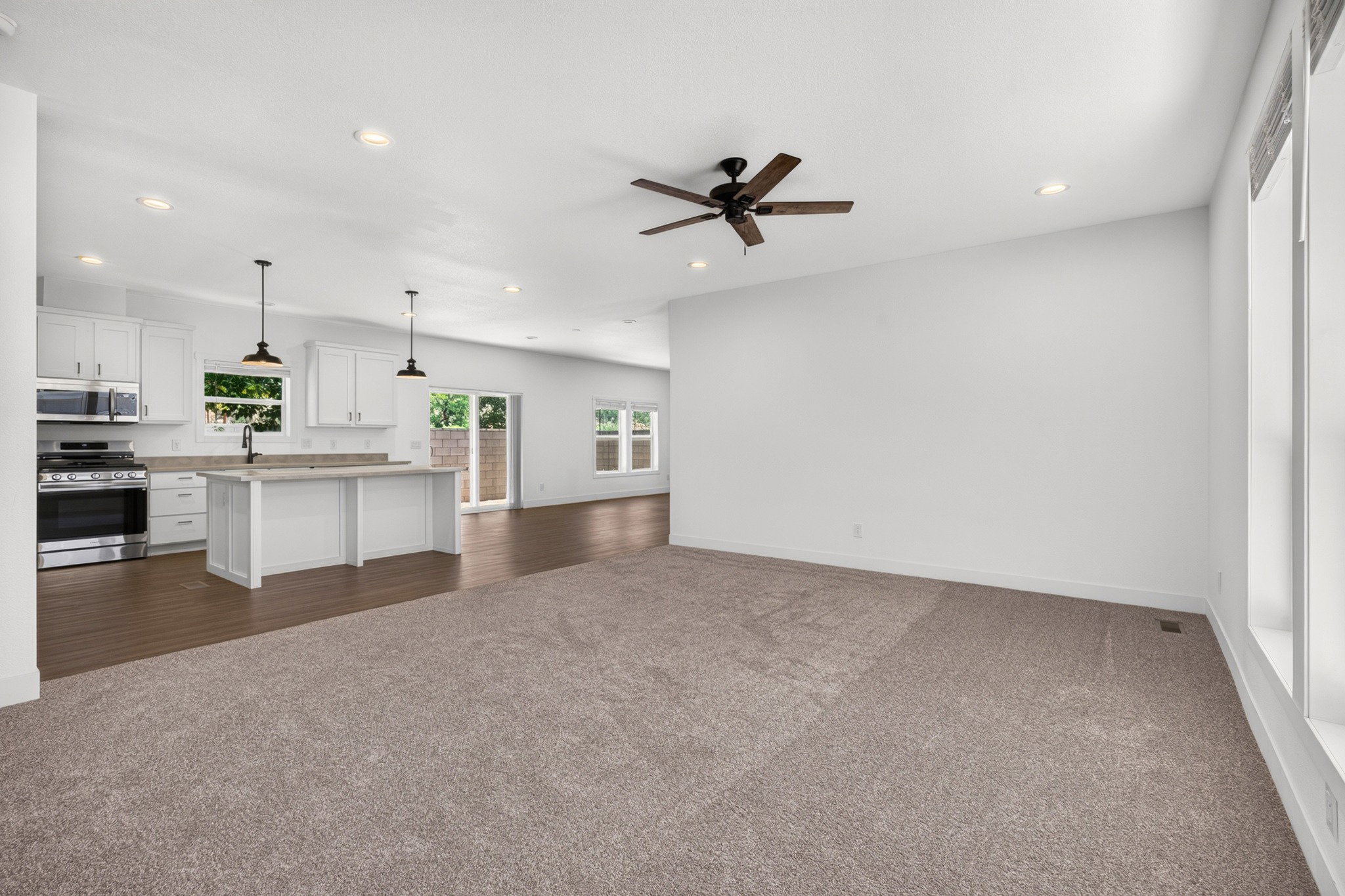Open-concept living space featuring a contemporary kitchen with white shaker cabinetry, stainless steel appliances, and a central island with countertop seating