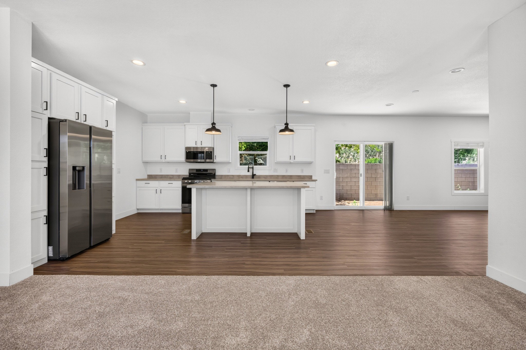 Open-concept kitchen featuring white cabinetry, stainless steel appliances, an island with seating, and wood-finish flooring