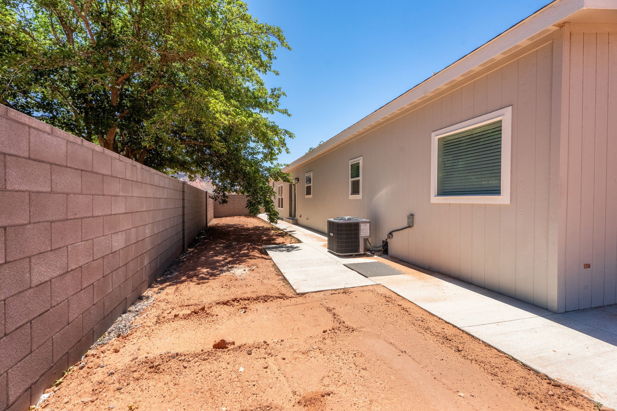 Exterior side yard featuring a concrete walkway, light-colored stucco siding, and a block perimeter wall