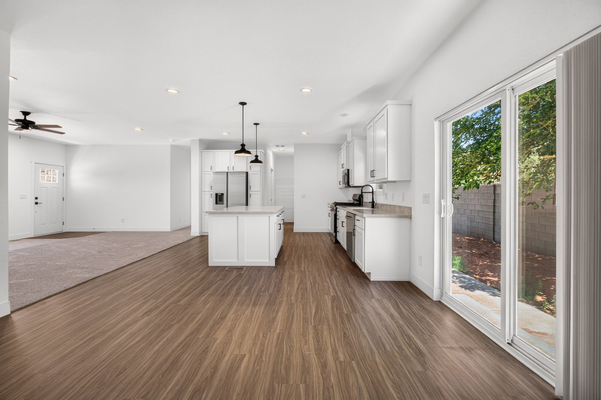 Modern kitchen featuring white cabinetry, a central island with pendant lighting, stainless steel appliances, and wood-finish flooring
