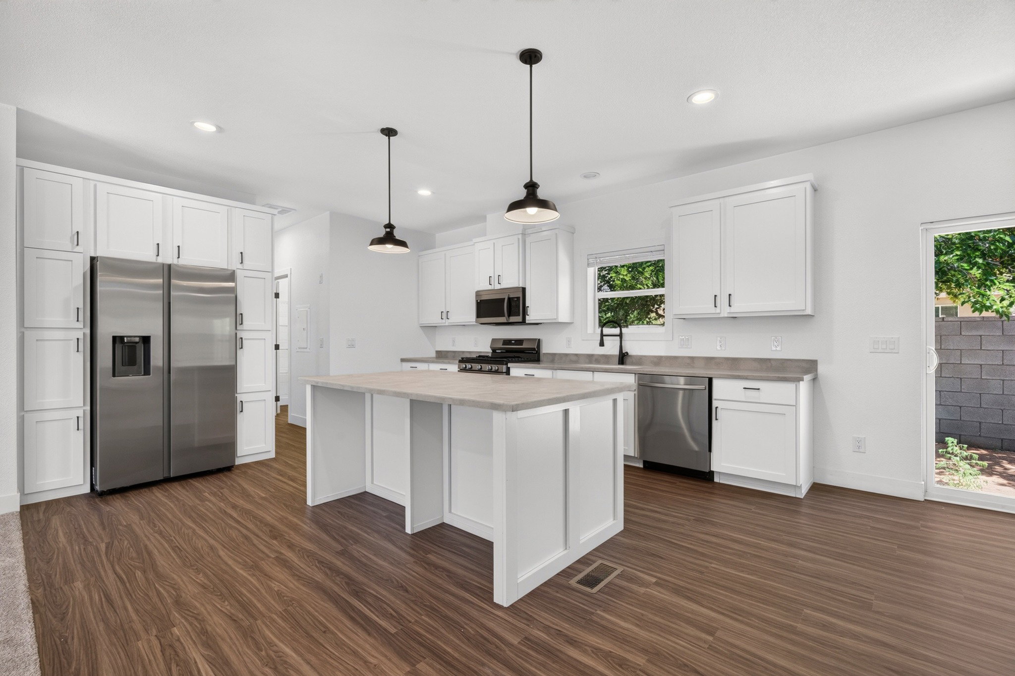 Modern kitchen featuring an expansive center island with countertop seating, stainless steel appliances, white cabinetry with black hardware, wood-finish flooring, and recessed lighting