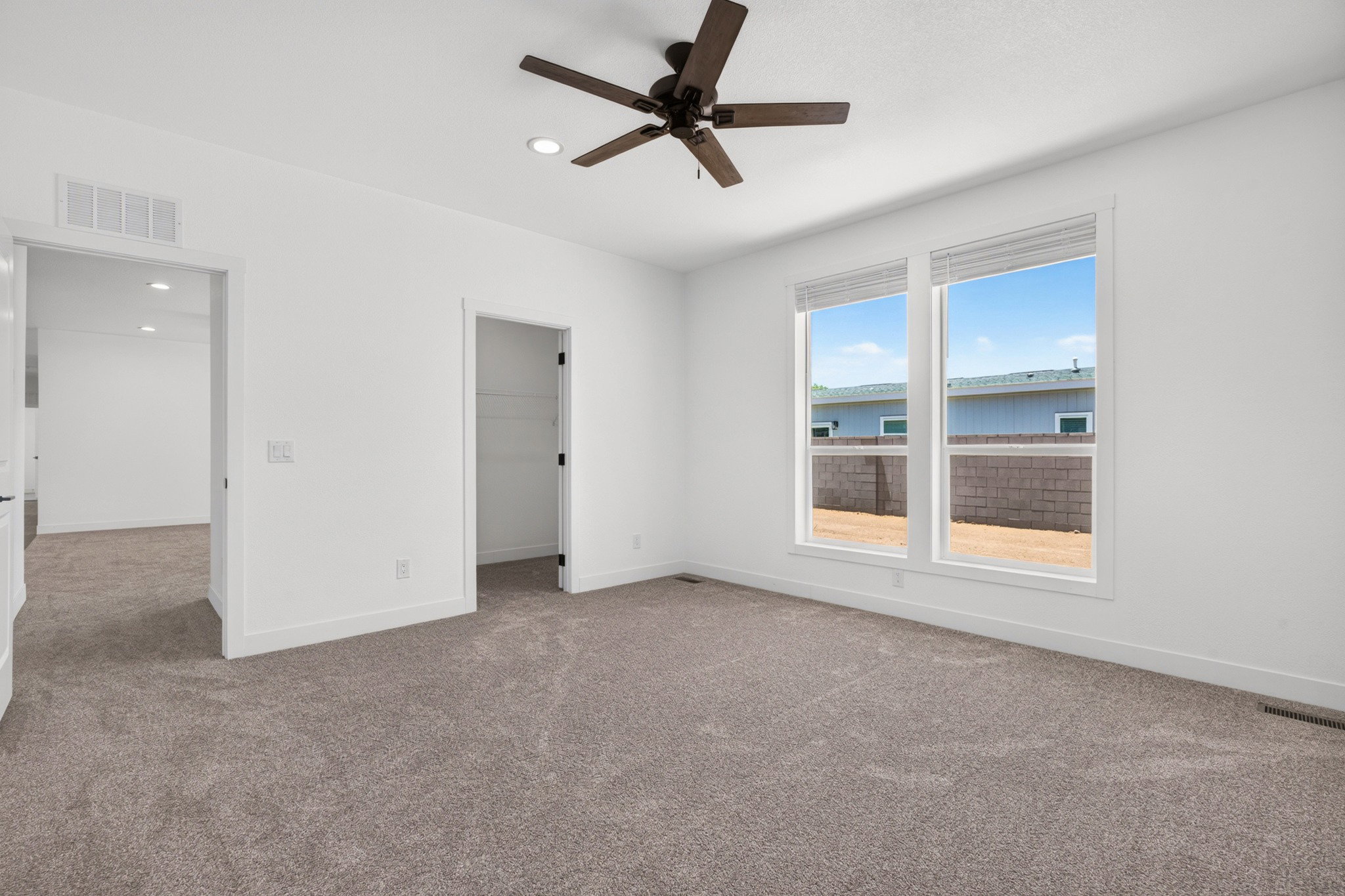 Spacious room featuring neutral carpeting, a dark-toned ceiling fan, recessed lighting, and two large windows with blinds