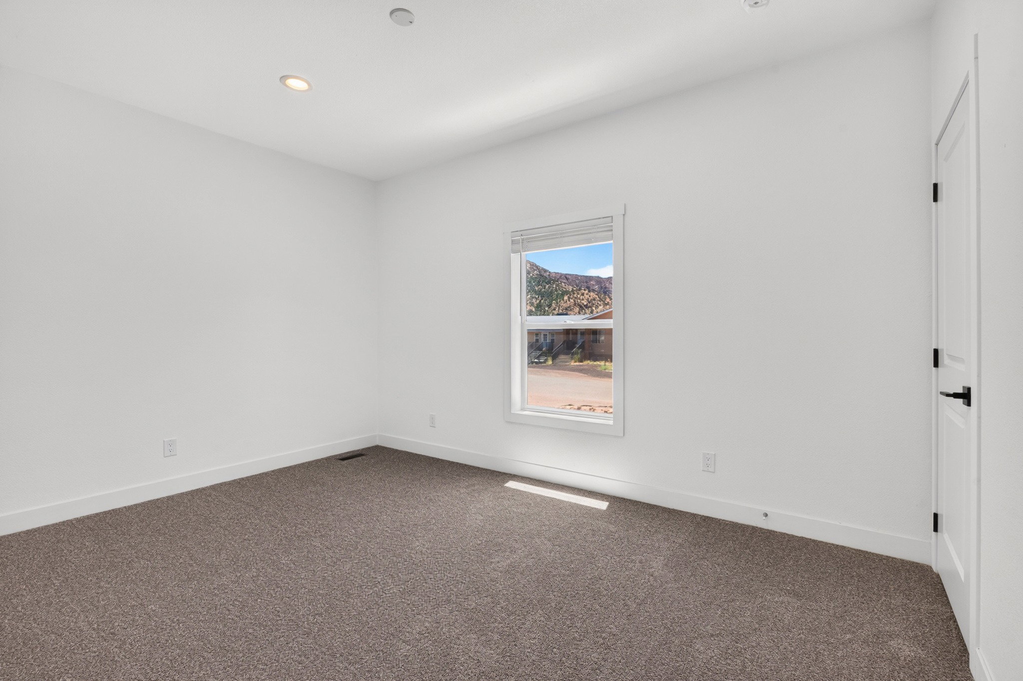 Carpeted room with white walls, recessed lighting, and a window framing a mountain backdrop