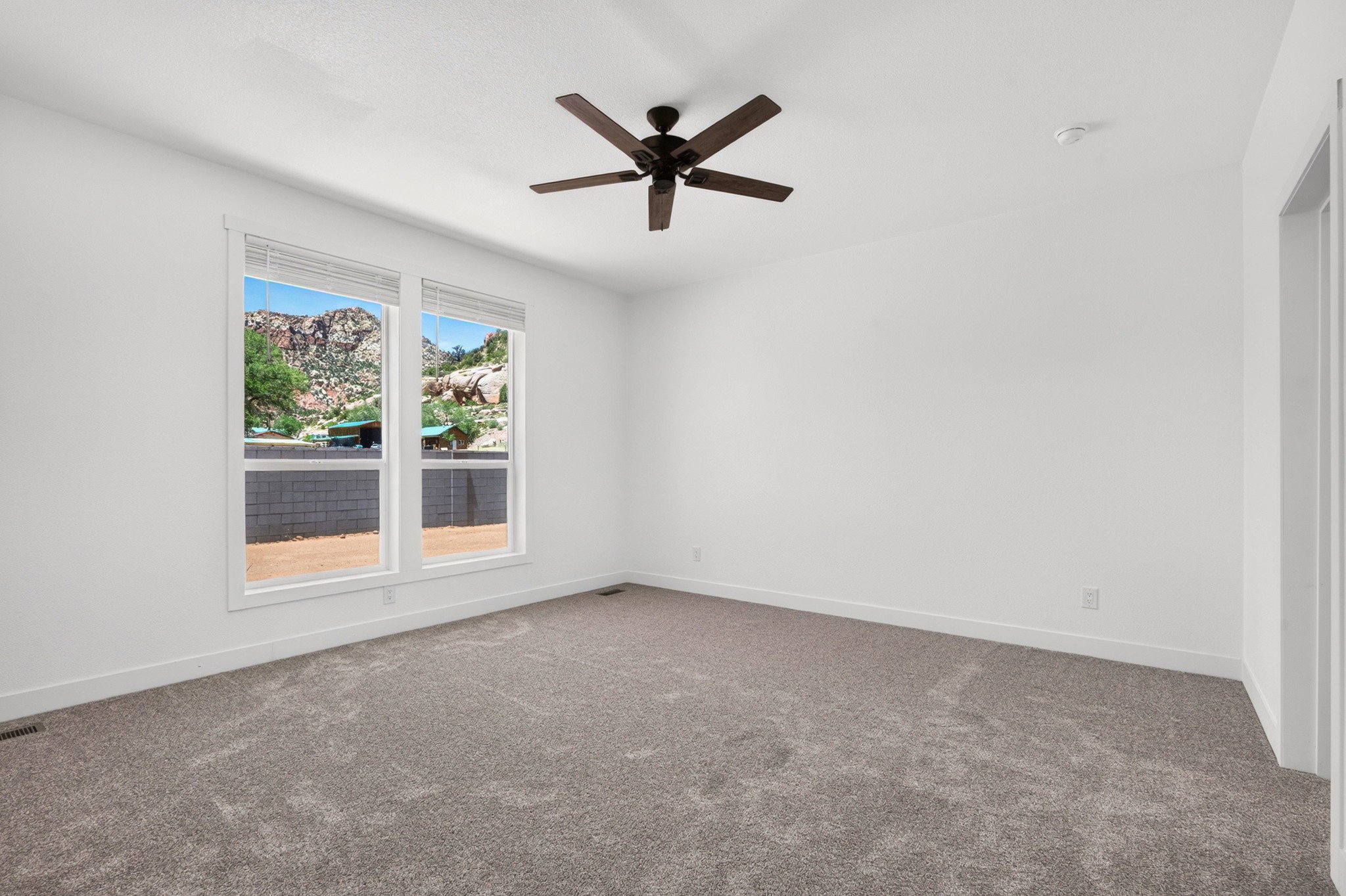 Spacious room featuring neutral carpeting, white walls, and a dark-toned ceiling fan
