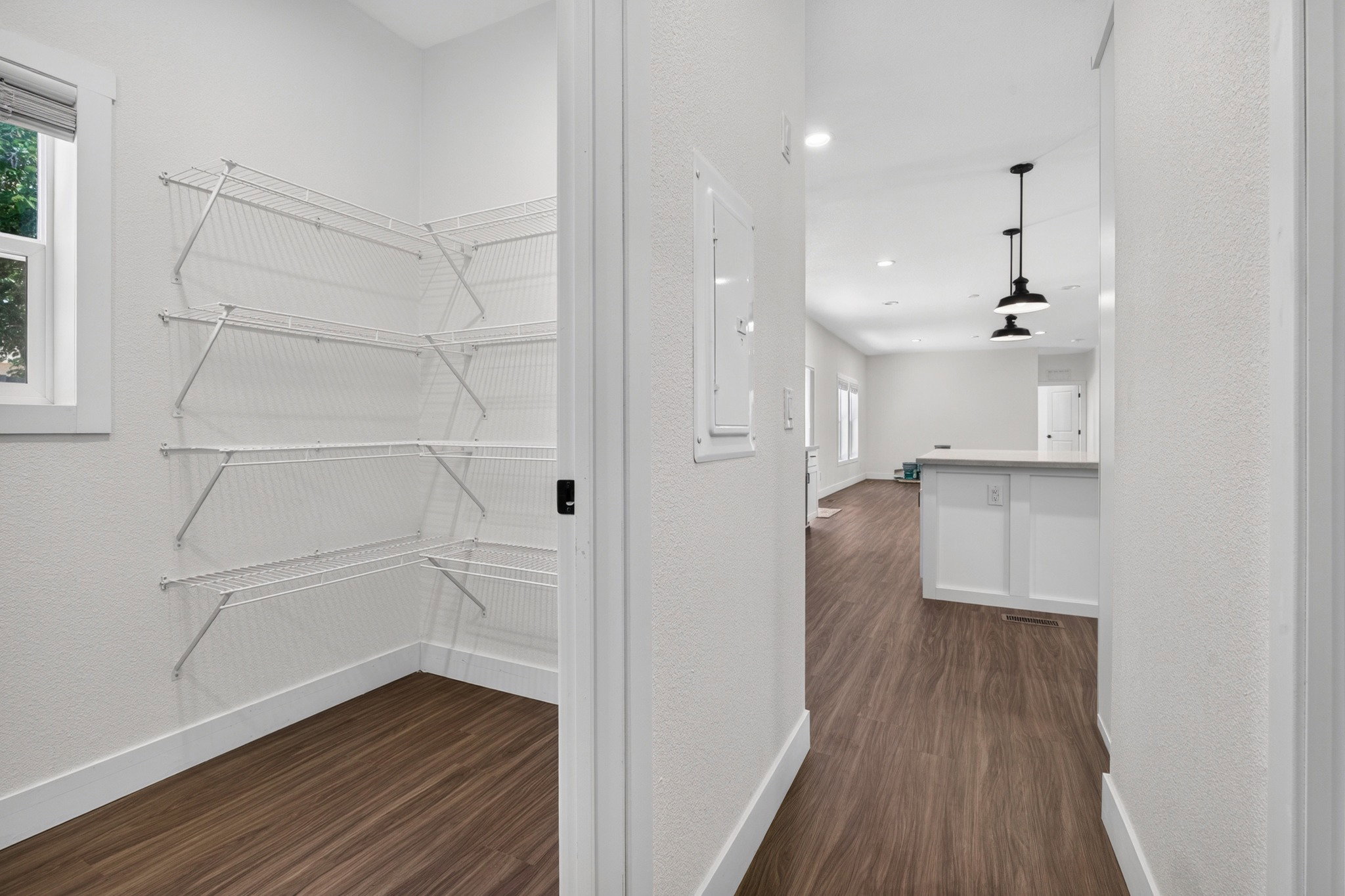 Spacious pantry with wire shelving and a window, featuring wood-finish flooring