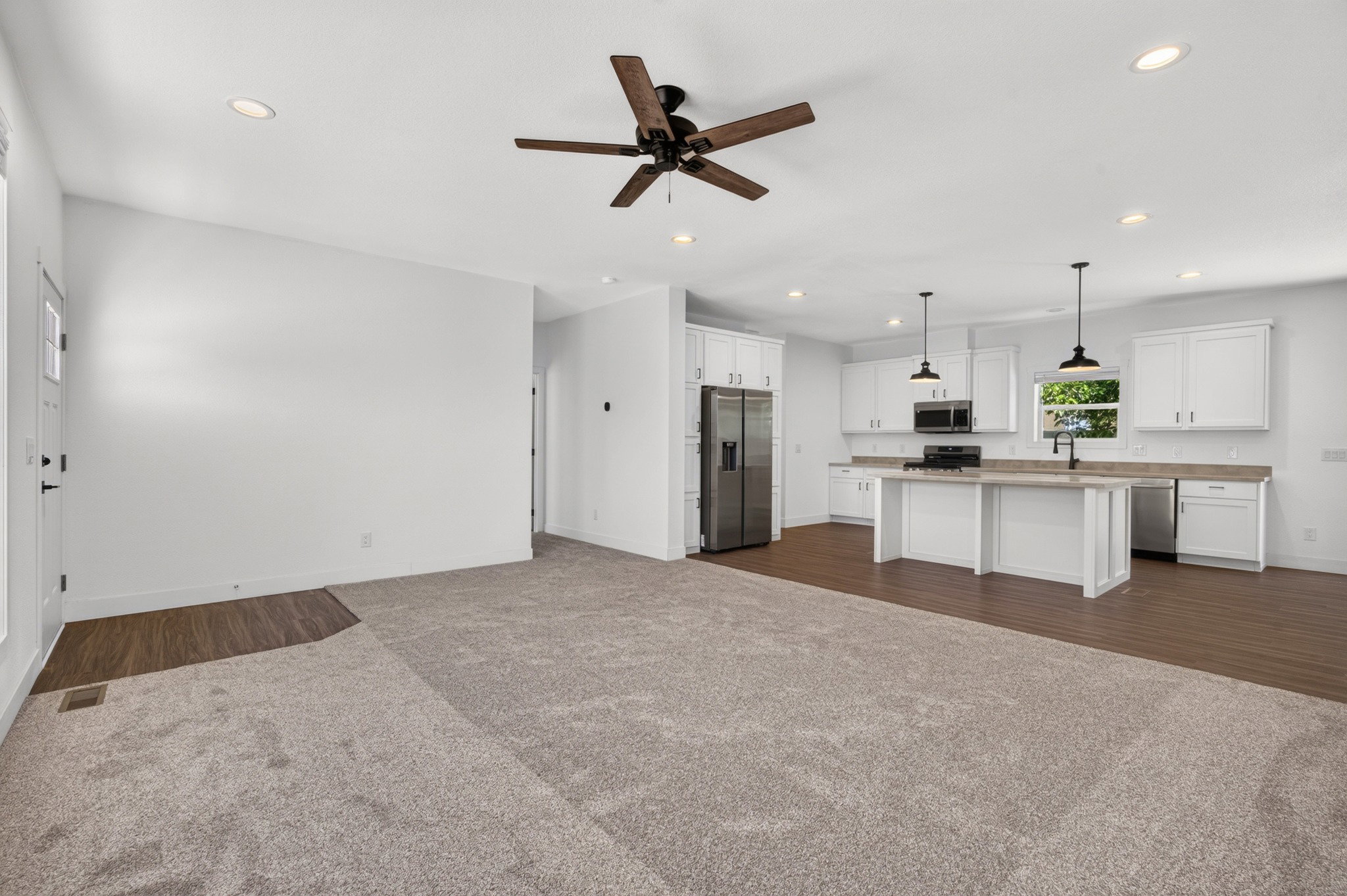 Open-concept living space featuring a contemporary kitchen with white cabinetry, stainless steel appliances, and a central island with pendant lighting