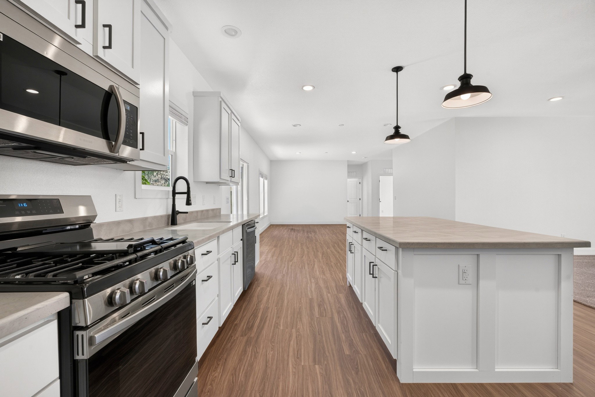 Kitchen featuring white cabinetry with dark hardware, stainless steel appliances, a gas range, and a kitchen island with pendant lighting