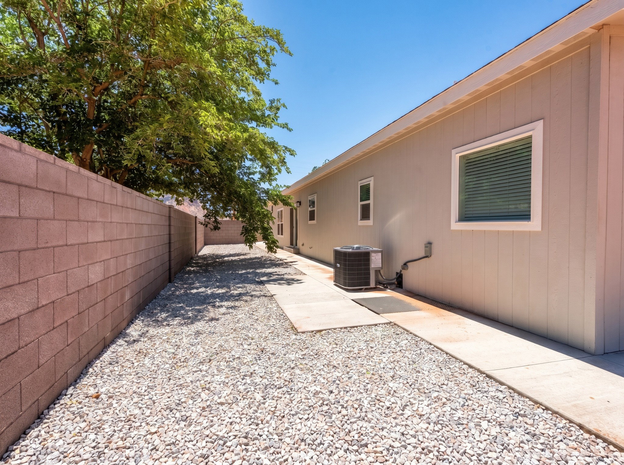 Side yard featuring a concrete block wall, gravel landscaping, and a concrete walkway