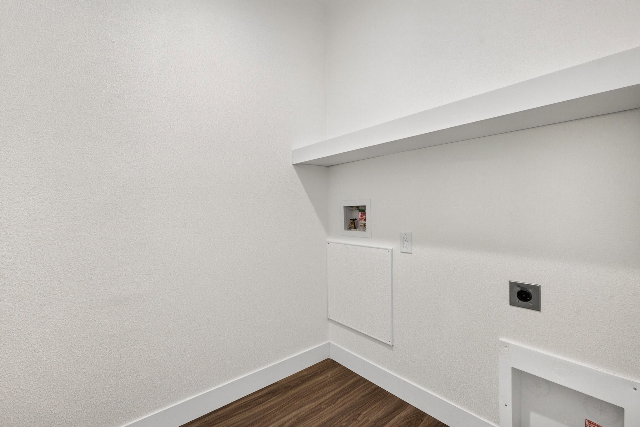 Dedicated utility space featuring a built-in white shelf, wood-finish flooring, and crisp white baseboards