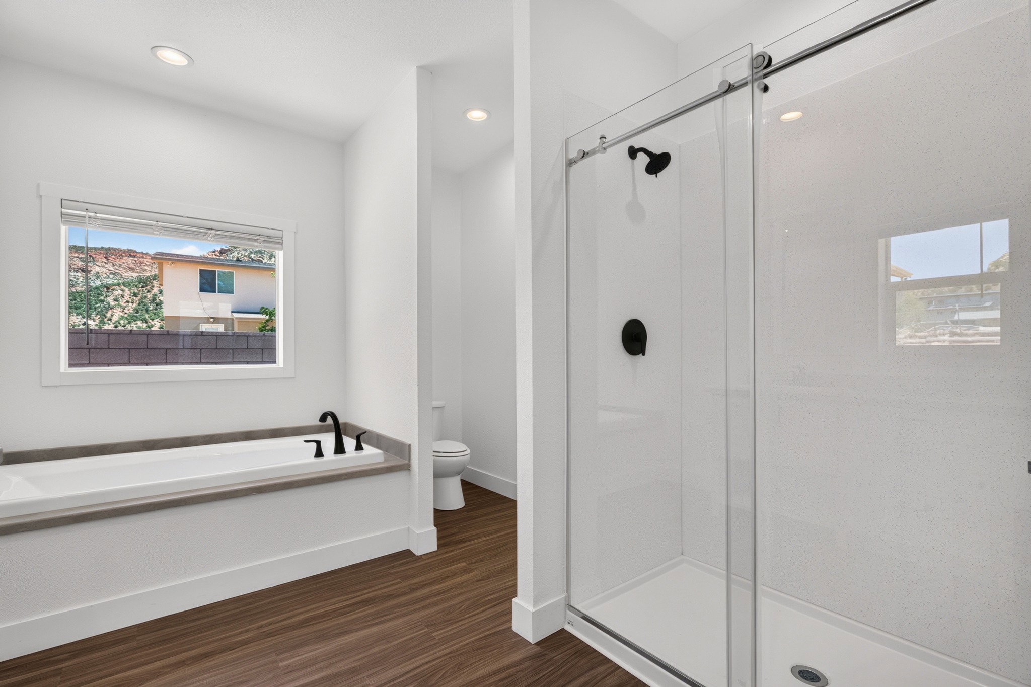 Modern bathroom featuring a soaking tub with matte black fixtures, a separate glass-enclosed shower with matte black hardware, recessed lighting, and wood-finish flooring