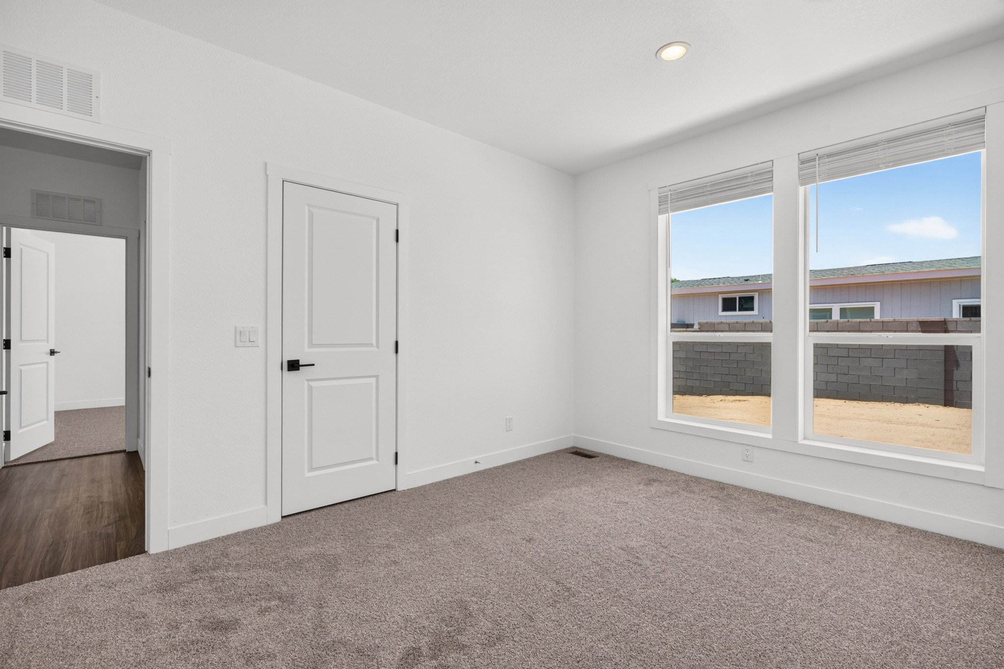 Light-filled room featuring neutral-toned carpet, recessed lighting, and a white interior door with matte black hardware