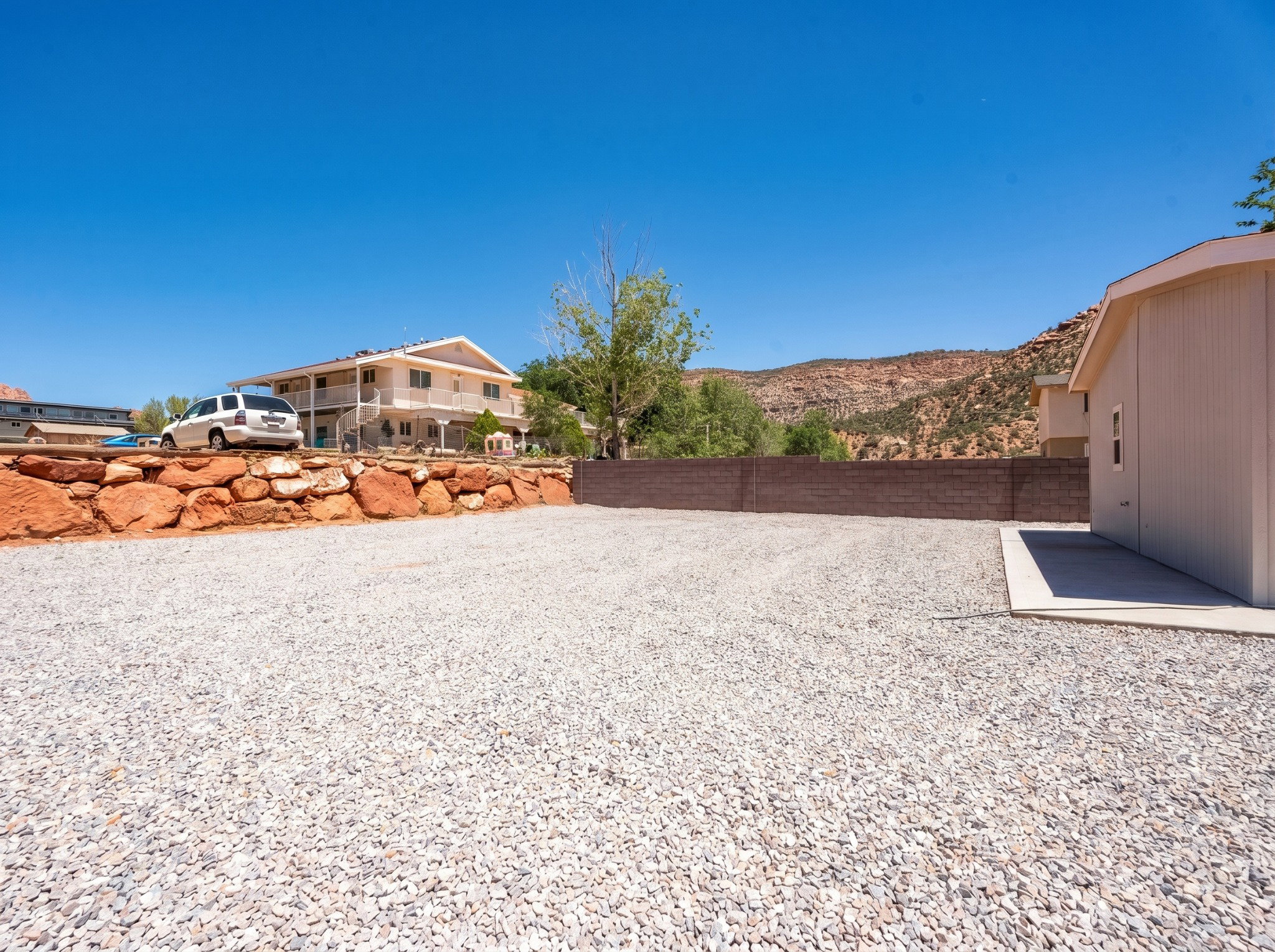 Expansive gravel area featuring a concrete slab, a block retaining wall, and an additional storage structure