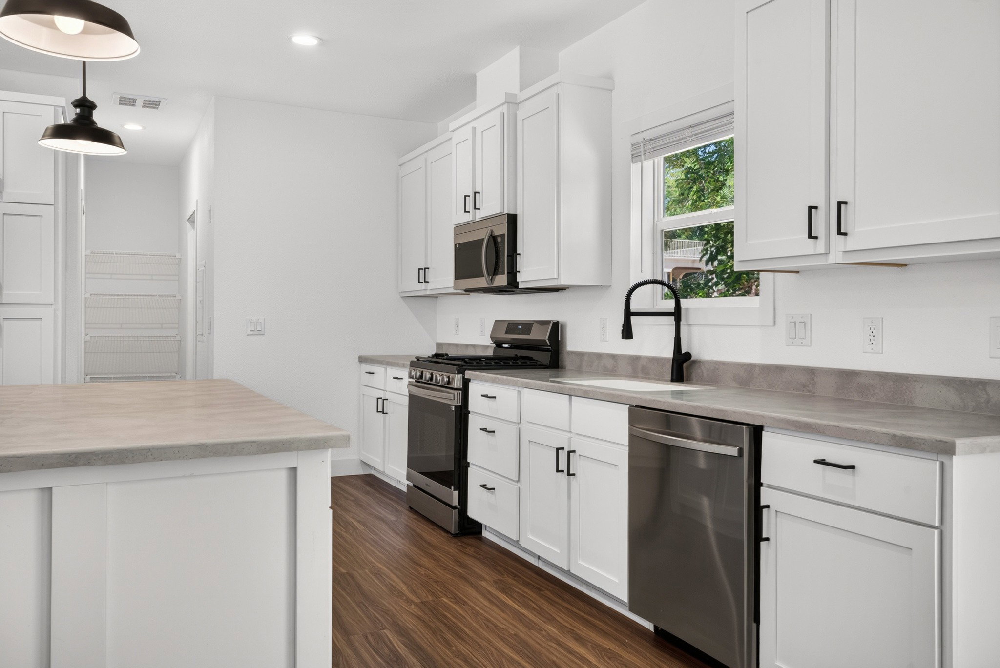 Bright kitchen featuring white shaker cabinetry, stainless steel appliances, dark wood-finish flooring, and light-toned countertops