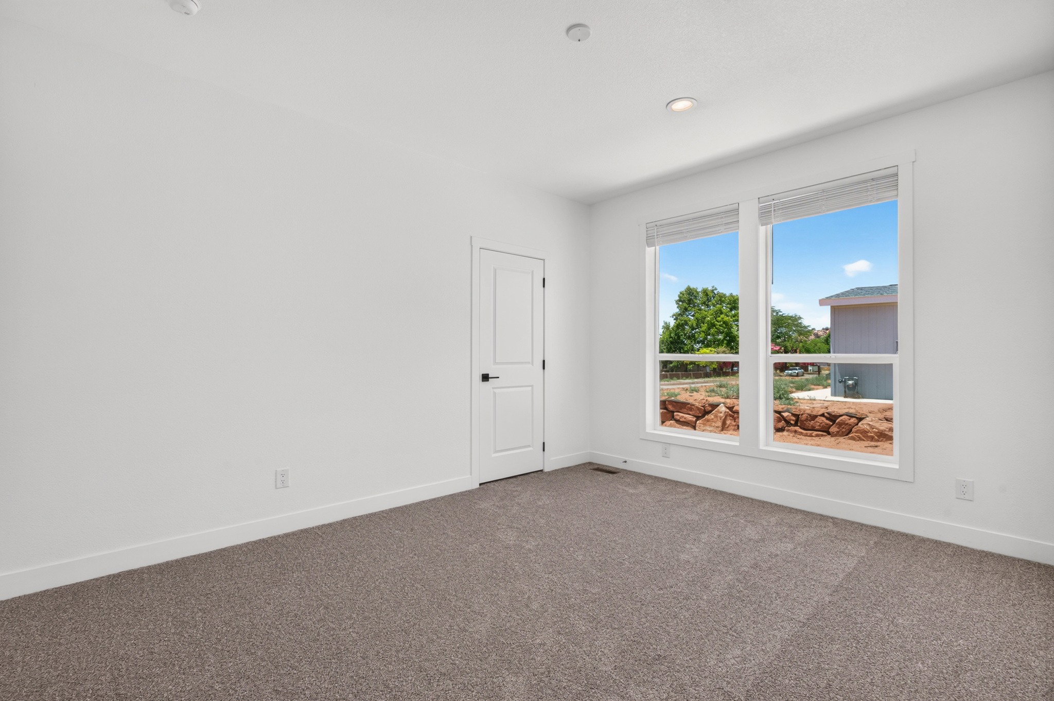 Carpeted room with white walls, two large windows, and a white two-panel door with black hardware