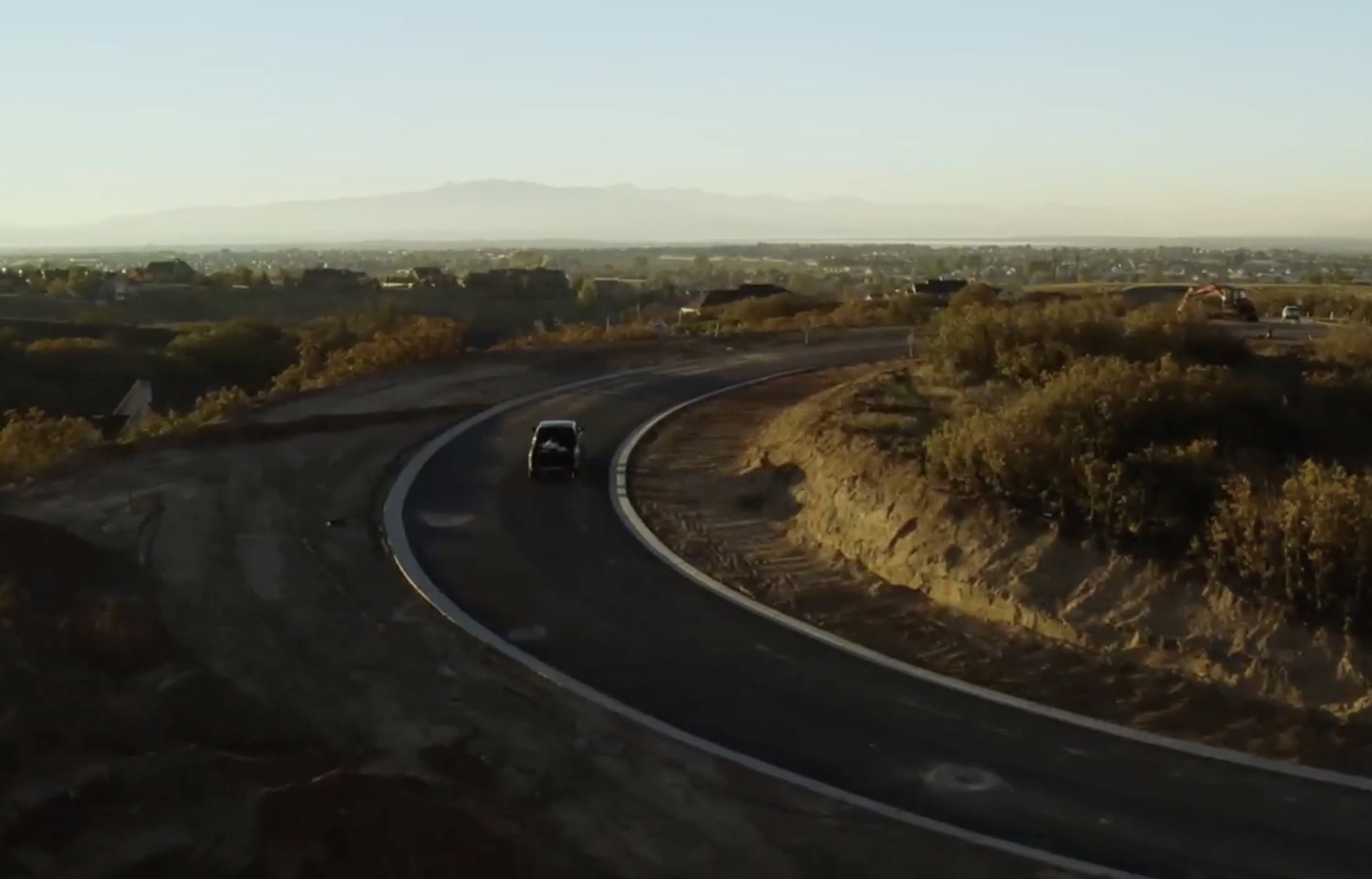 Curved paved road with concrete curbing, bordered by natural landscaping