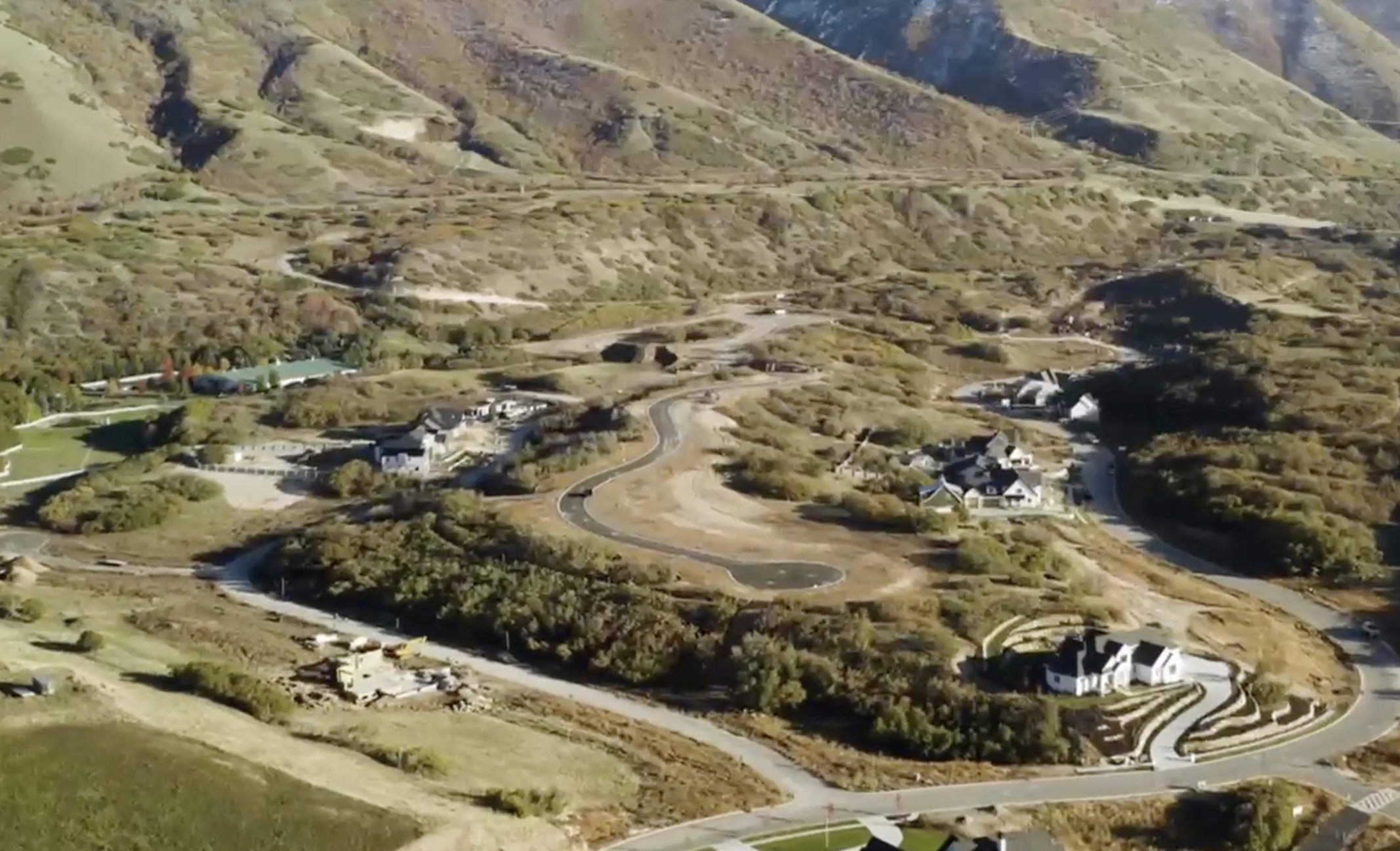 Expansive aerial showcasing multiple new construction homes and vacant lots nestled within a mountainous landscape