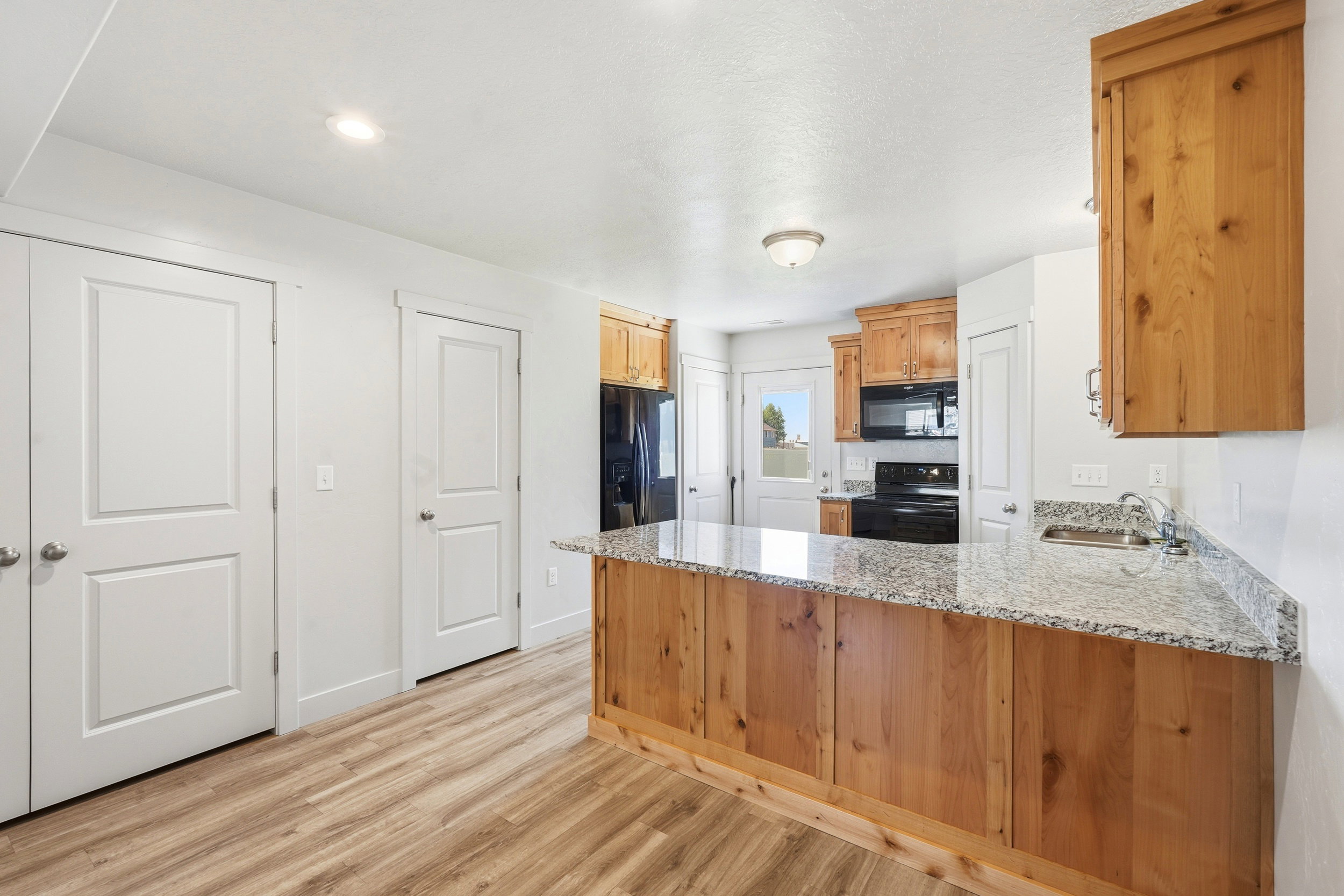 Kitchen featuring wood-finish cabinetry, granite-style countertops, stainless steel sink, black appliances, and wood-finish flooring