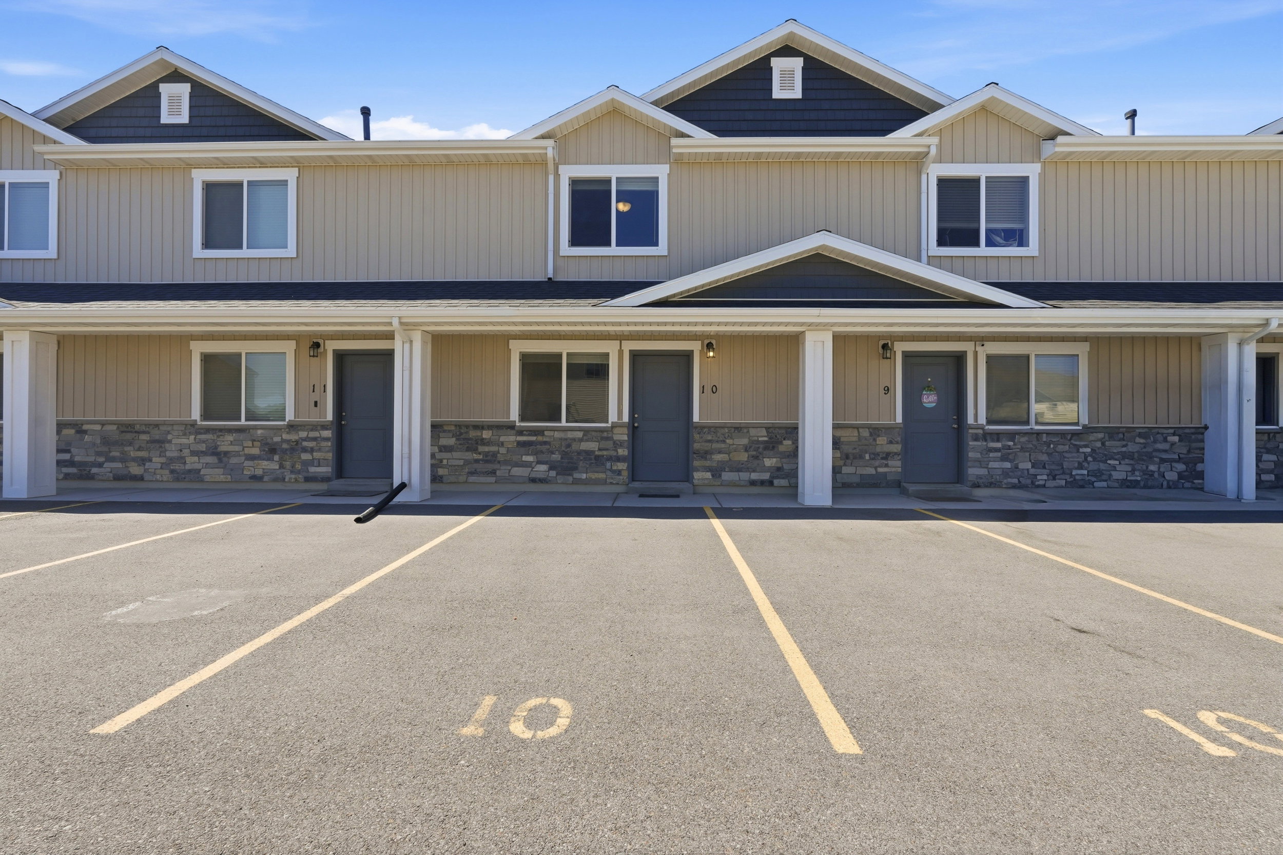 Multi-unit residential facade featuring beige vertical siding, dark gray horizontal siding in the gables, and stone veneer accents
