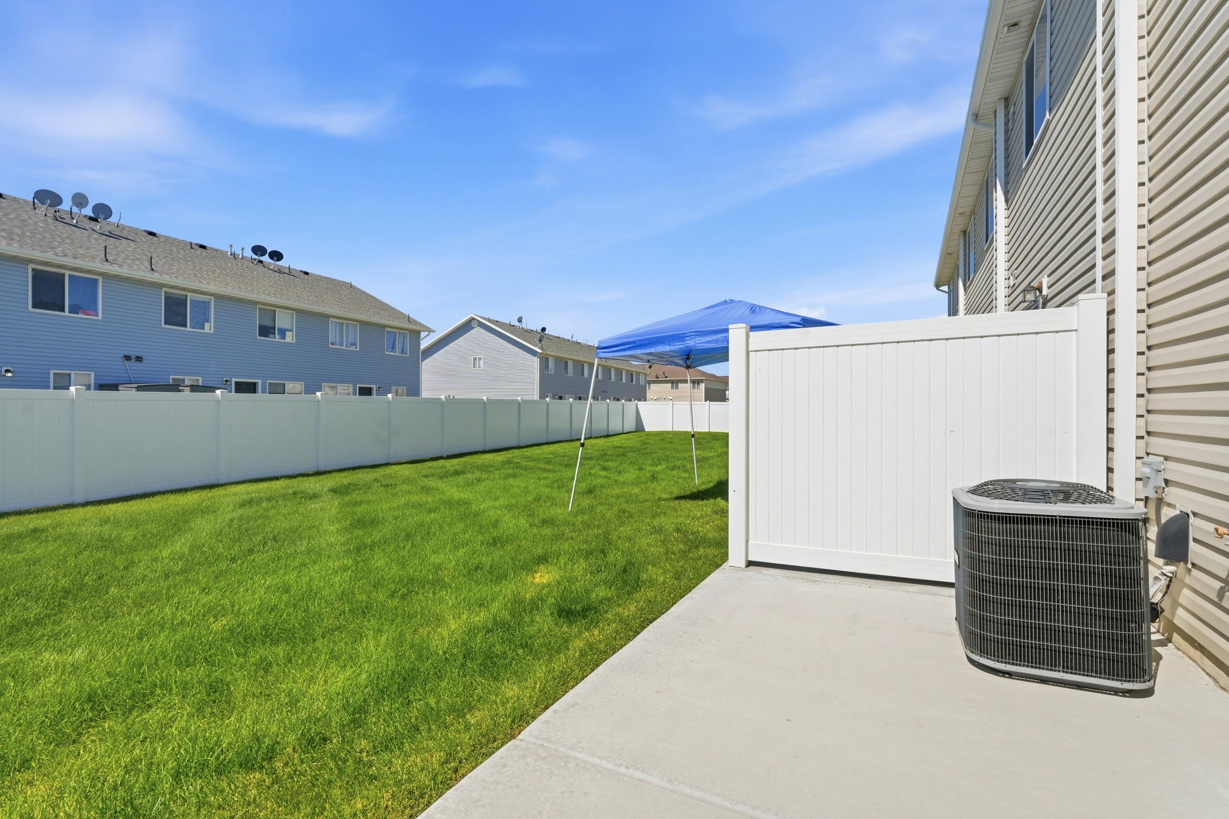 Expansive green space featuring a concrete patio, vinyl fencing, and tan horizontal siding
