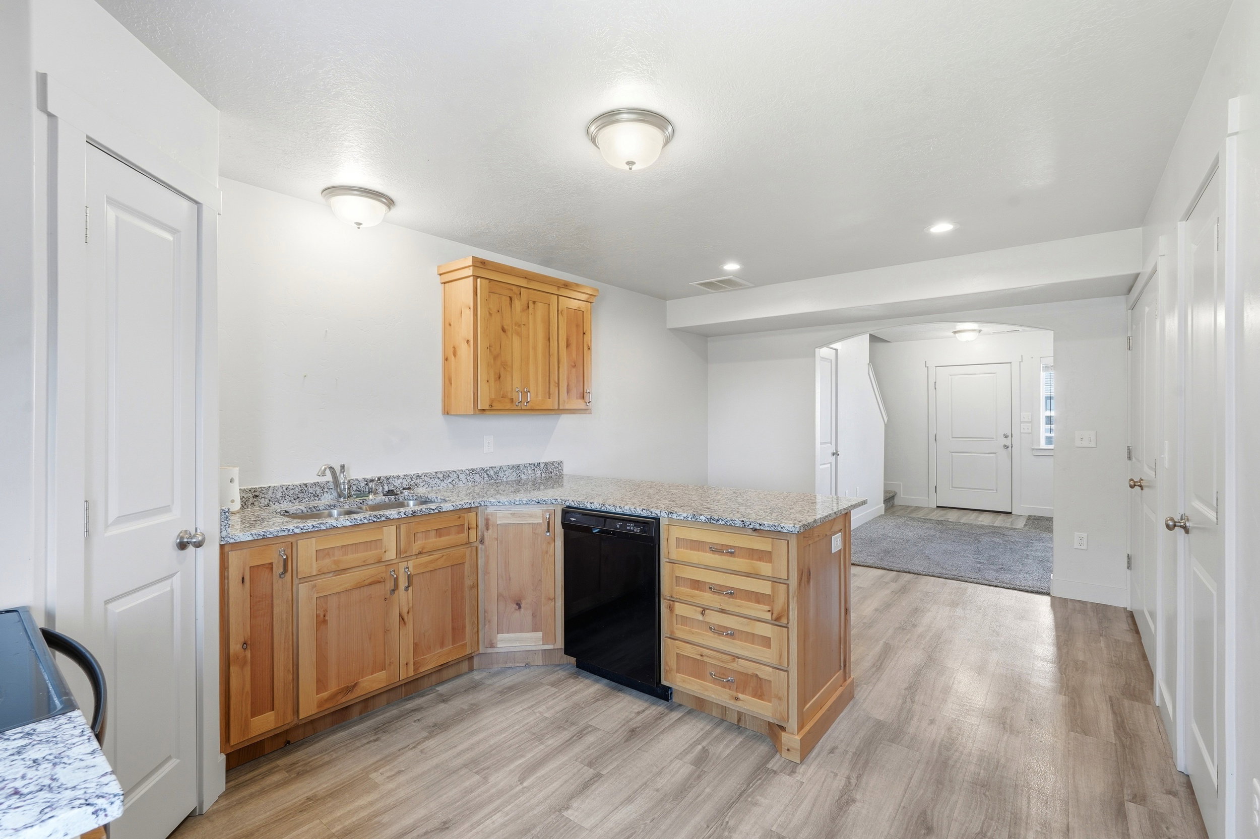 Kitchen featuring wood-finish cabinetry, granite-style countertops, a stainless steel sink, and a black built-in dishwasher