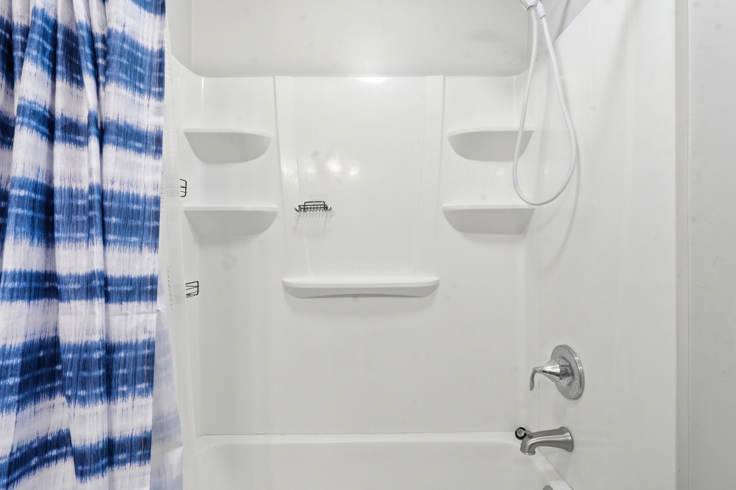 White fiberglass tub-shower combination featuring integrated shelving